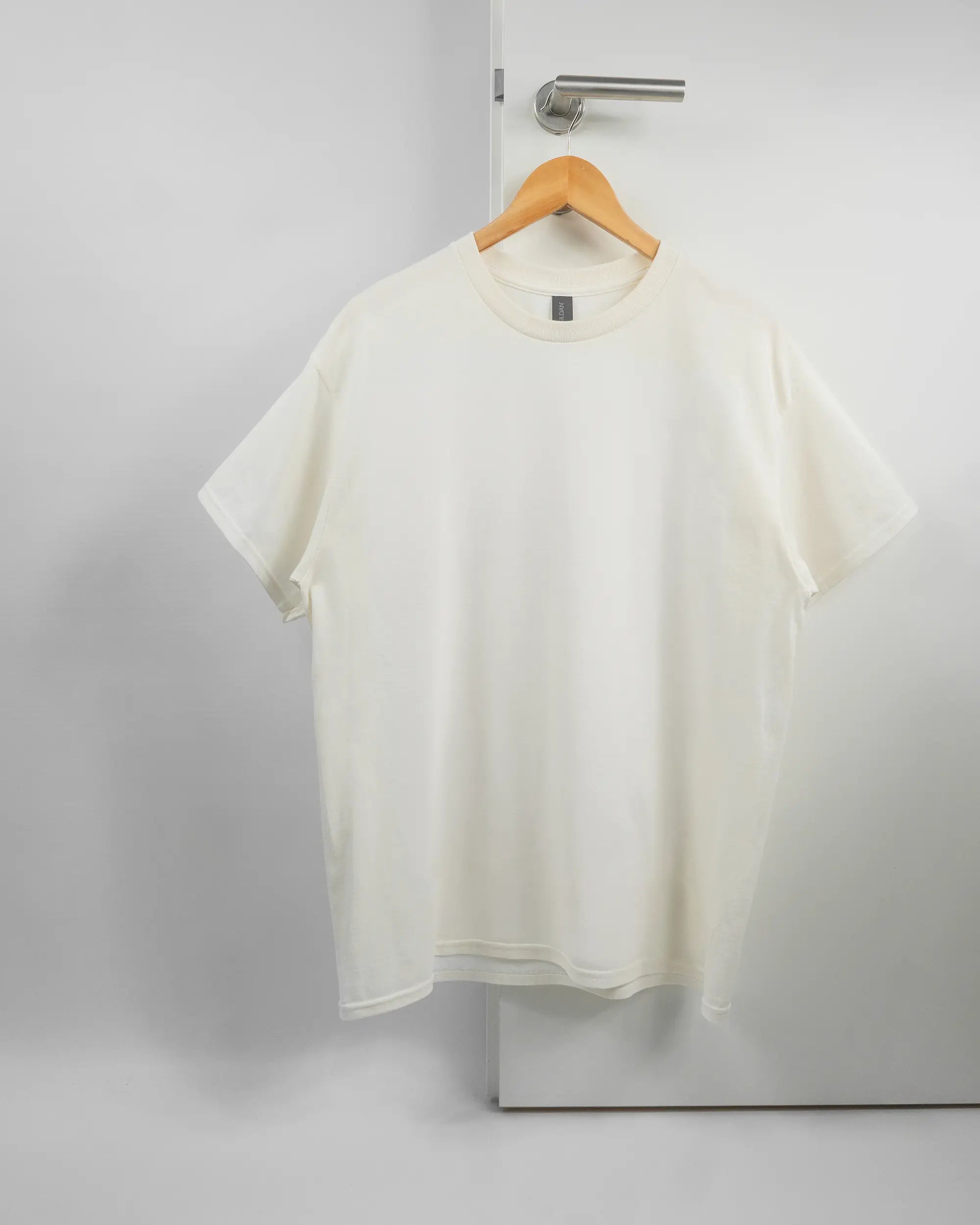 Vorderseite des Basic Unisex T-Shirt Regular von Maondo ohne Motiv in der Farbe White und in der Größe L auf einem Bügel an der Türklinke aufgehängt