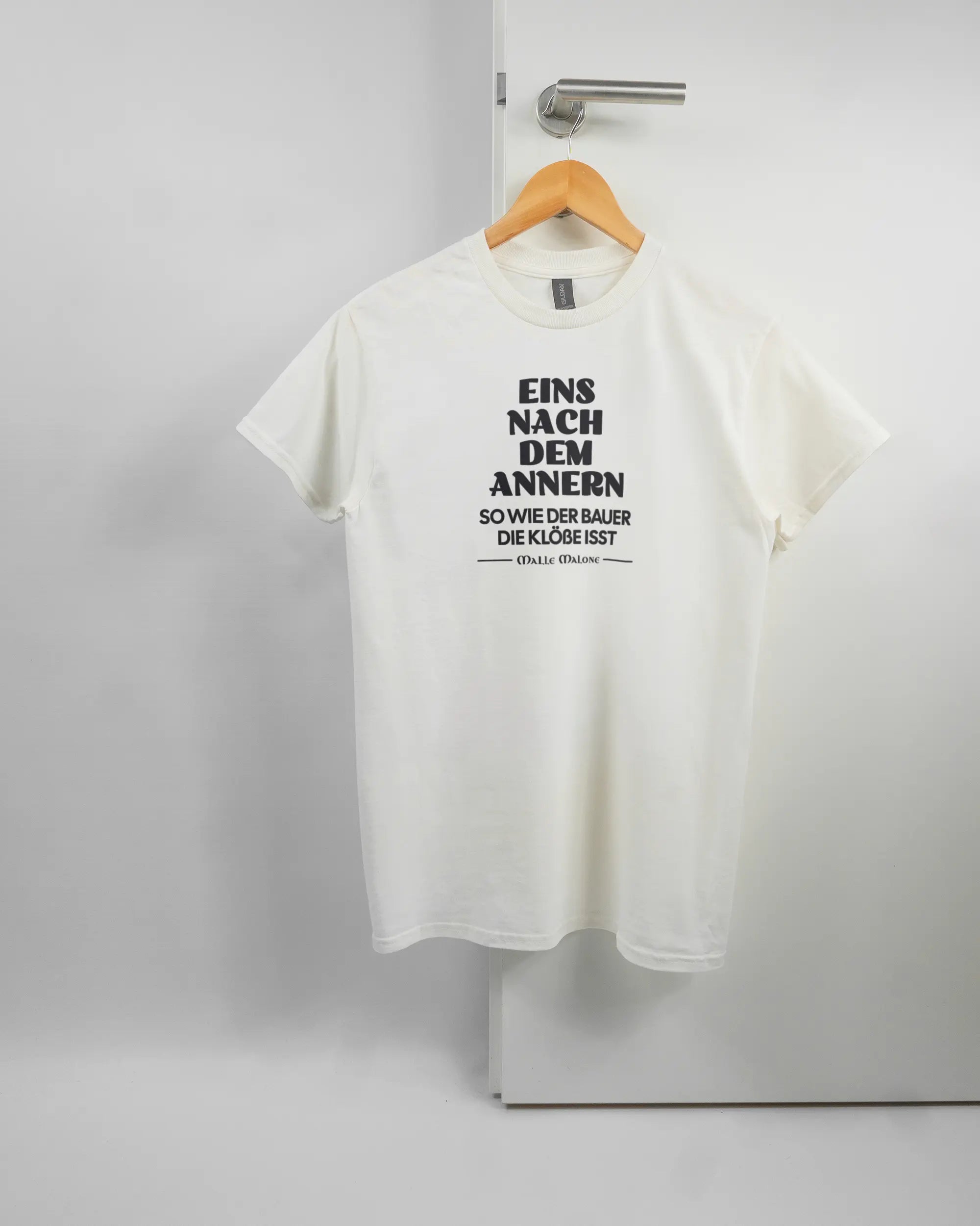 Vorderseite des Basic Unisex T-Shirt Regular von Maondo mit dem Design Eins nach dem Annern in der Farbe White und in der Größe S auf einem Bügel an der Türklinke aufgehängt