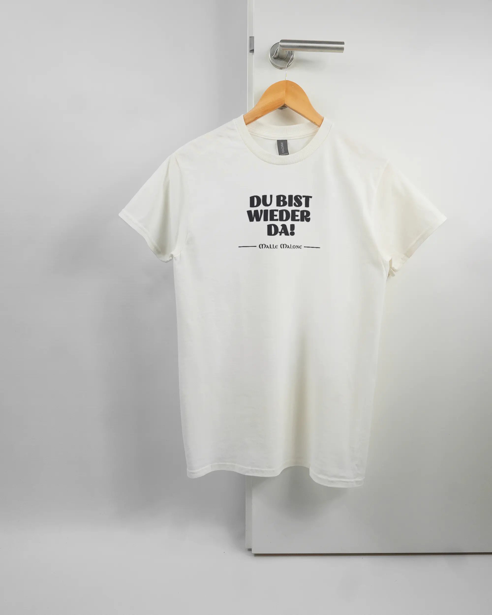 Vorderseite des Basic Unisex T-Shirt Regular von Maondo mit dem Design Wieder da in der Farbe White und in der Größe S auf einem Bügel an der Türklinke aufgehängt