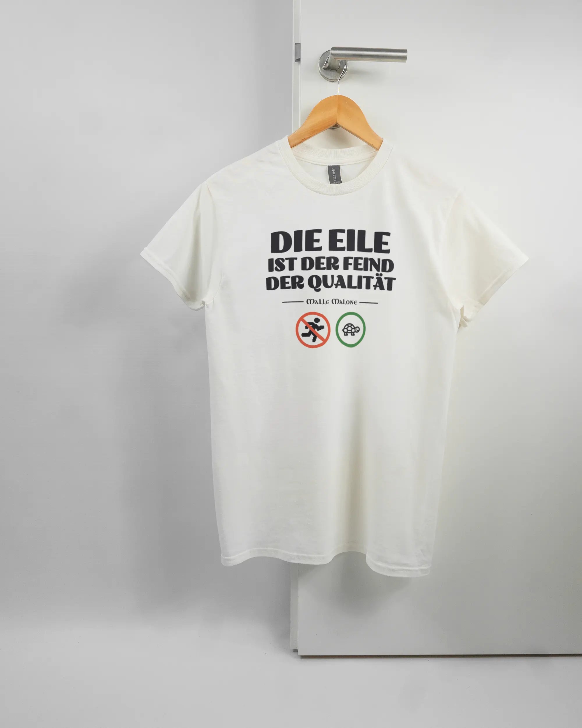 Vorderseite des Basic Unisex T-Shirt Regular von Maondo mit dem Design Keine Eile in der Farbe White und in der Größe S auf einem Bügel an der Türklinke aufgehängt