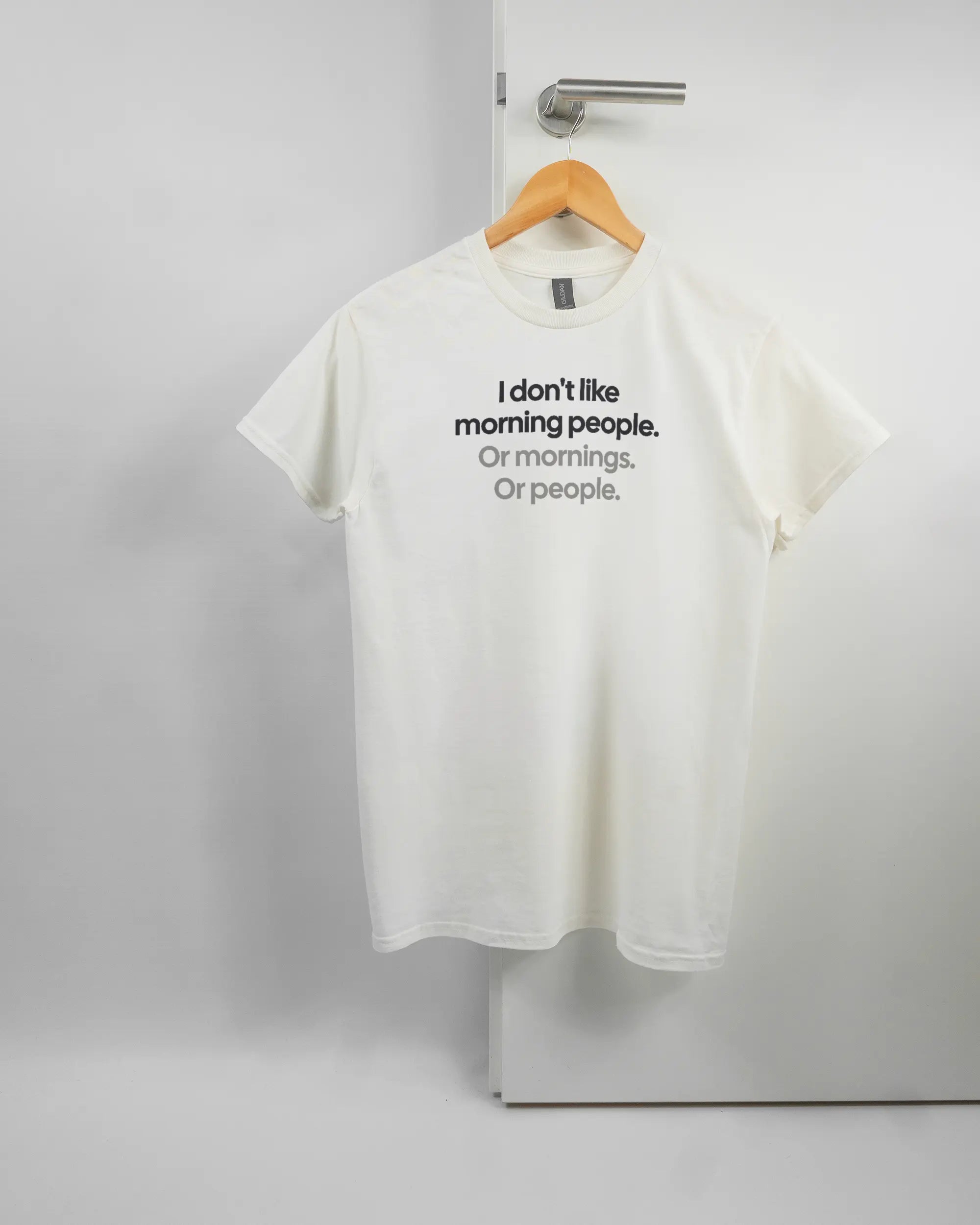 Vorderseite des Basic Unisex T-Shirt Regular von Maondo mit dem Design Morning Person in der Farbe White und in der Größe S auf einem Bügel an der Türklinke aufgehängt