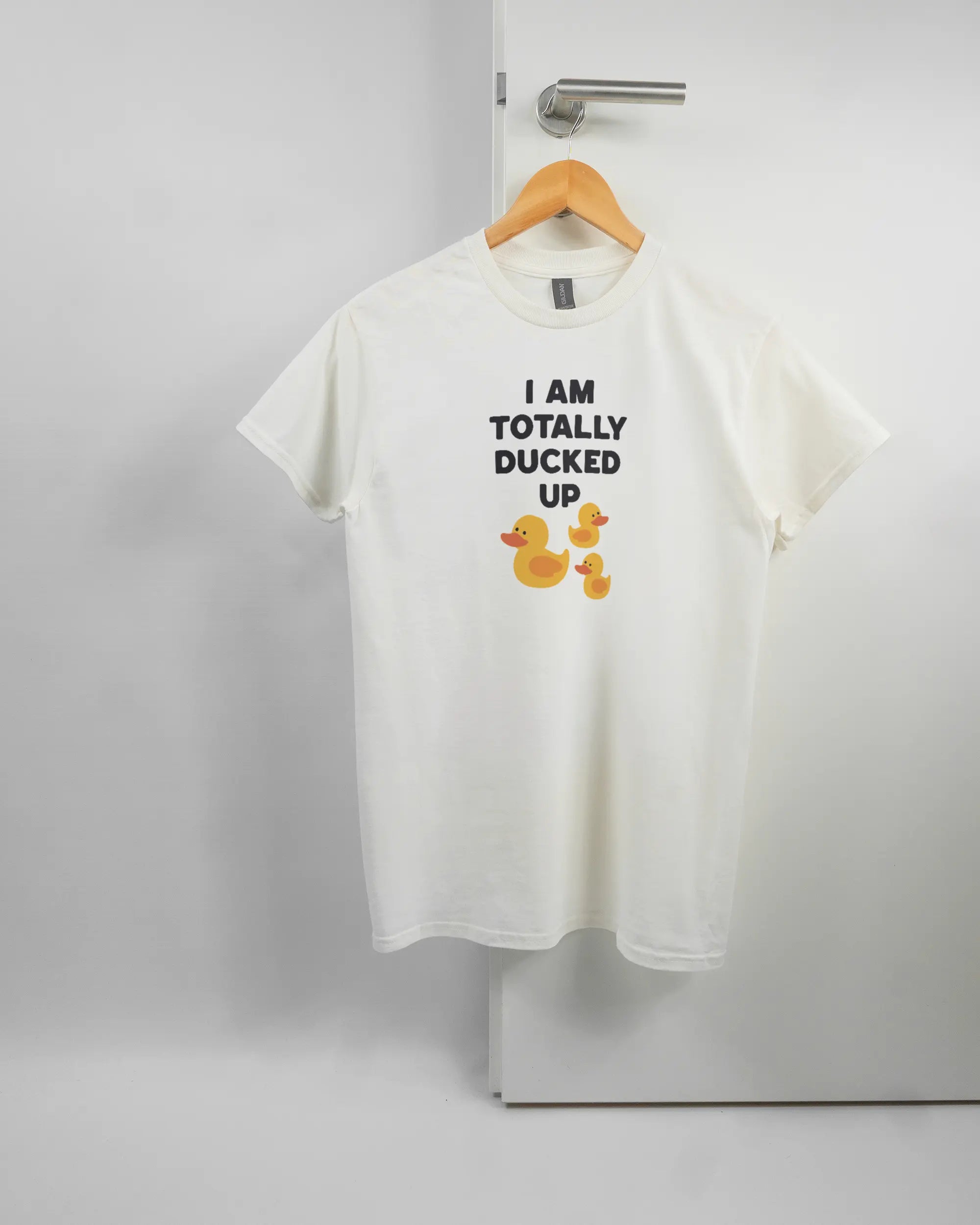 Vorderseite des Basic Unisex T-Shirt Regular von Maondo mit dem Design Ducked Up in der Farbe White und in der Größe S auf einem Bügel an der Türklinke aufgehängt