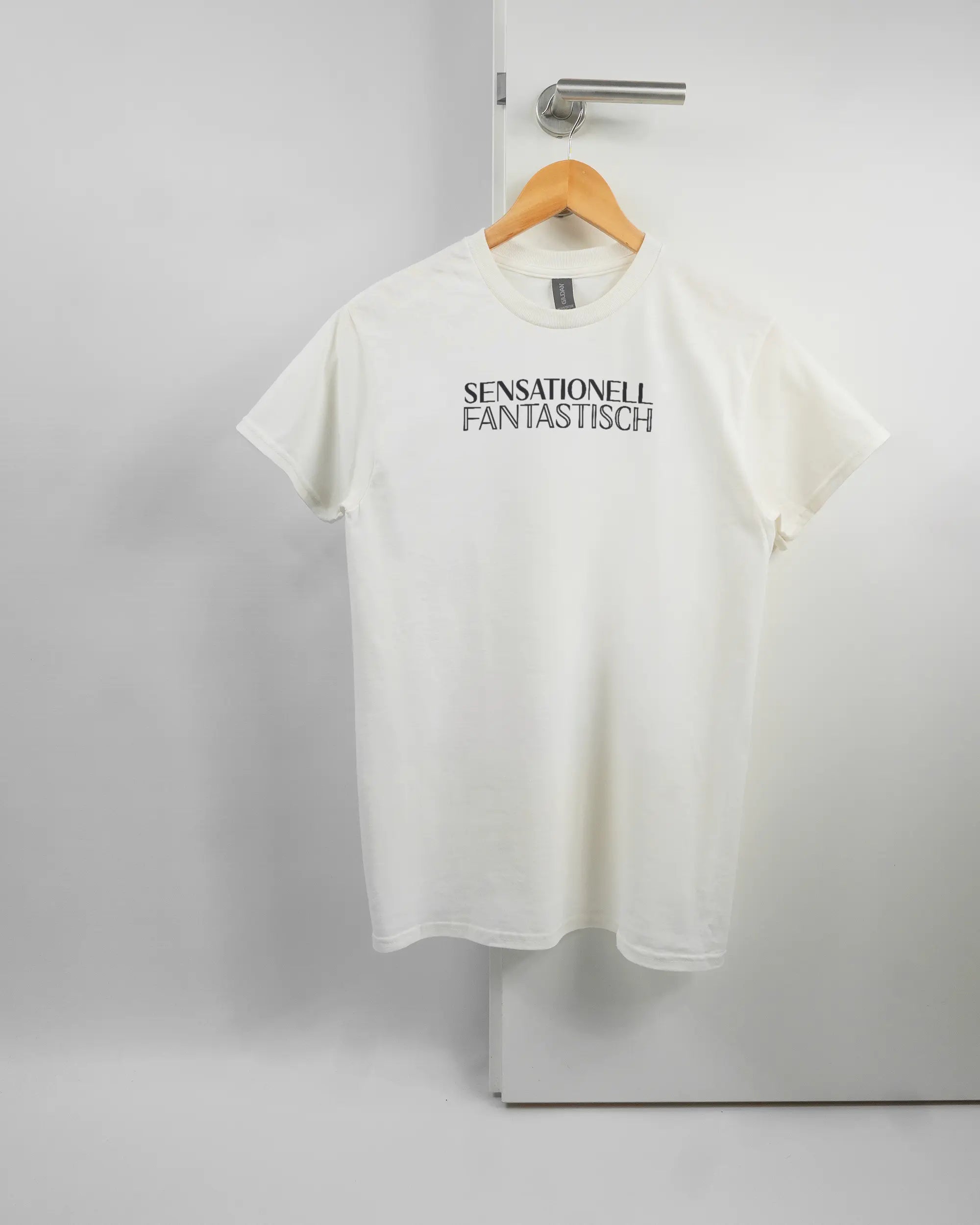 Vorderseite des Basic Unisex T-Shirt Regular von Maondo mit dem Design Sensationell in der Farbe White und in der Größe S auf einem Bügel an der Türklinke aufgehängt