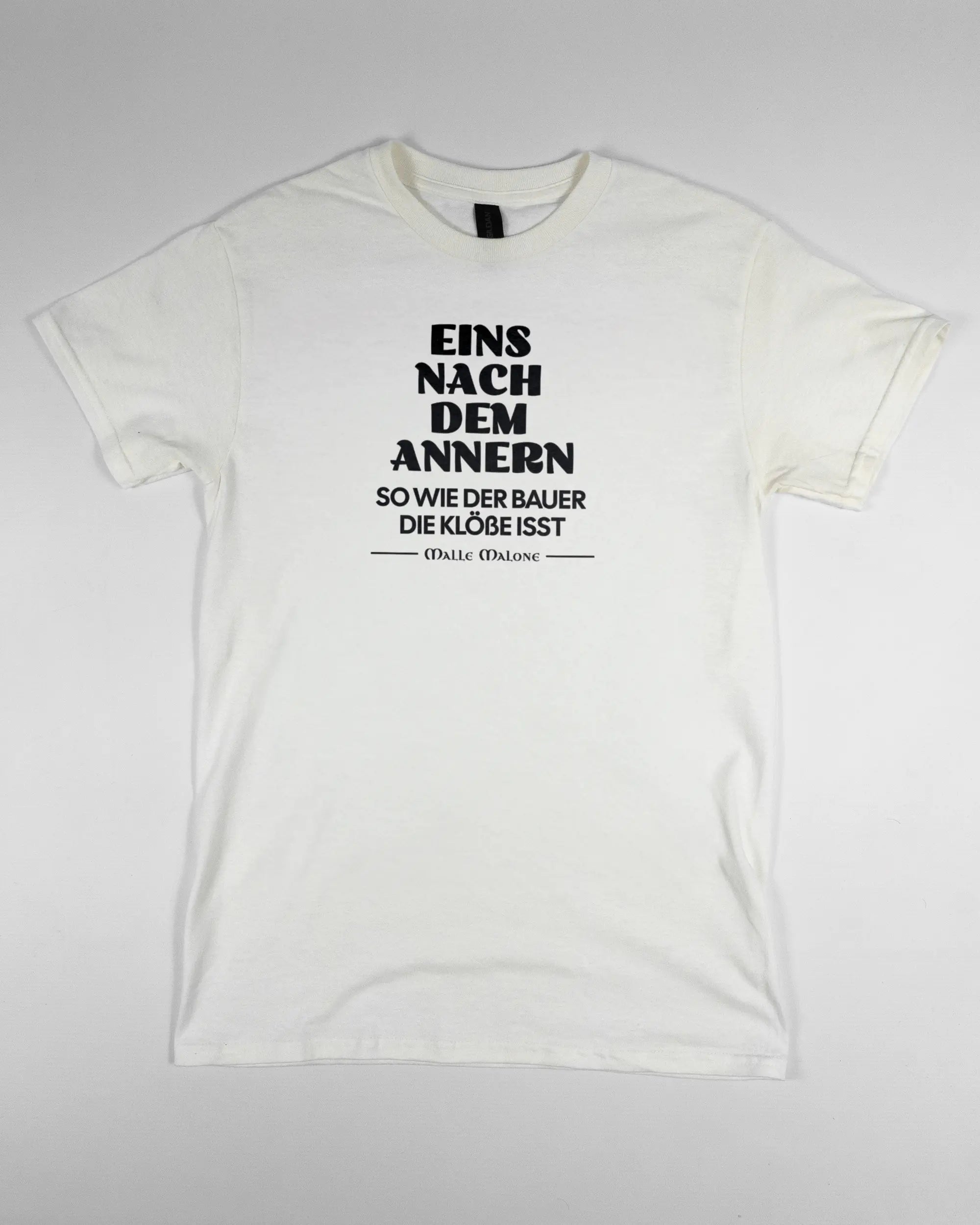Vorderseite des Basic Unisex T-Shirt Regular von Maondo mit dem Design Eins nach dem Annern in der Farbe White und in der Größe S flach auf den Boden gelegt