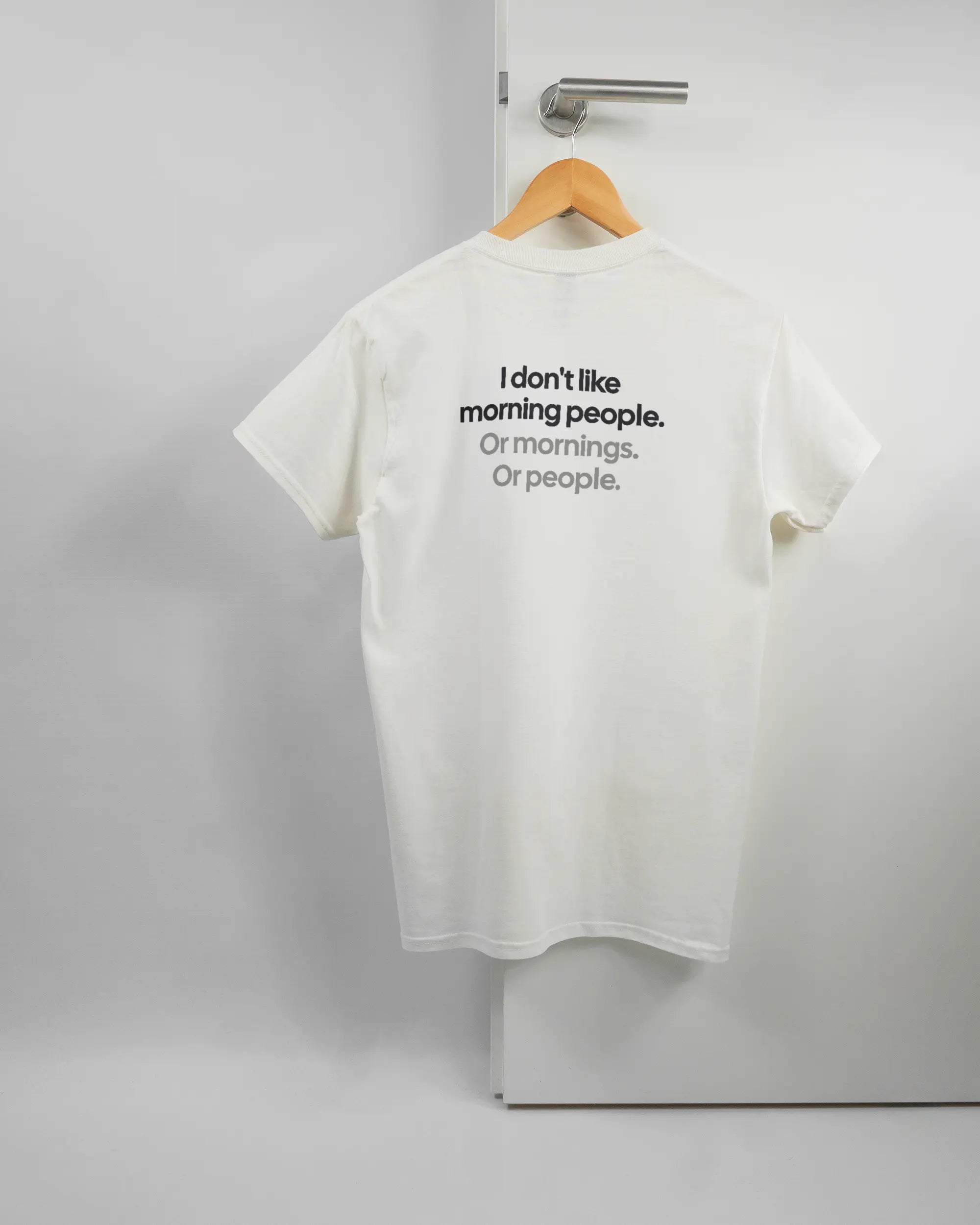 Rückseite des Basic Unisex T-Shirt Regular von Maondo mit dem Design Morning Person in der Farbe White und in der Größe S auf einem Bügel an der Türklinke aufgehängt