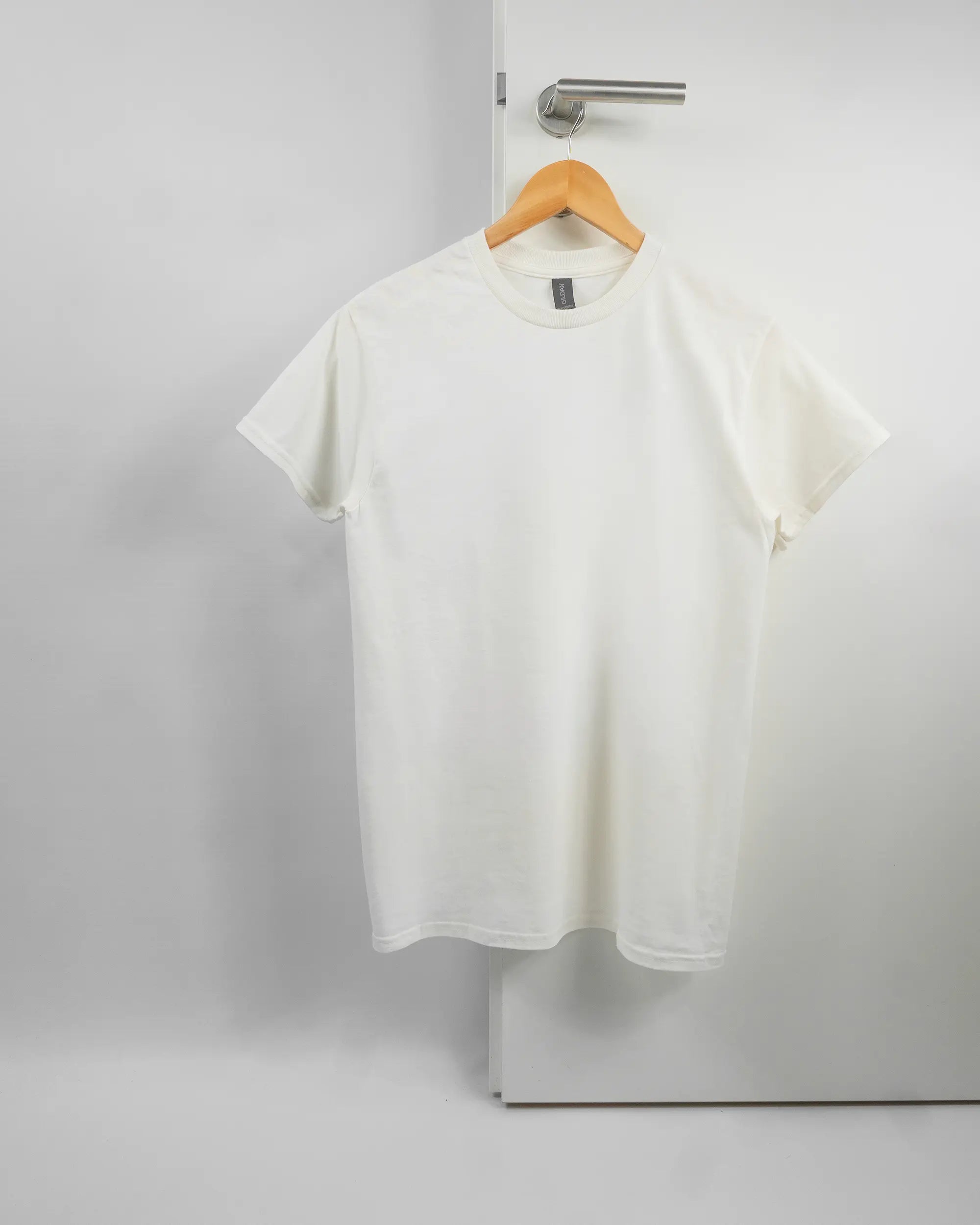 Vorderseite des Basic Unisex T-Shirt Regular von Maondo ohne Motiv in der Farbe White und in der Größe S auf einem Bügel an der Türklinke aufgehängt