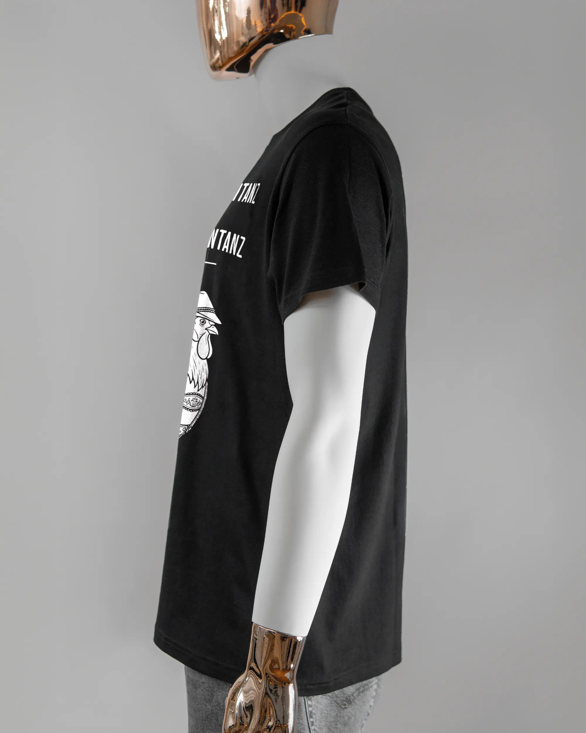 Seitenansicht des Basic Unisex T-Shirt Soft von Maondo mit dem Design Trachtentanz vorne in der Farbe Black und in der Größe L getragen von einer maskulinen Puppe