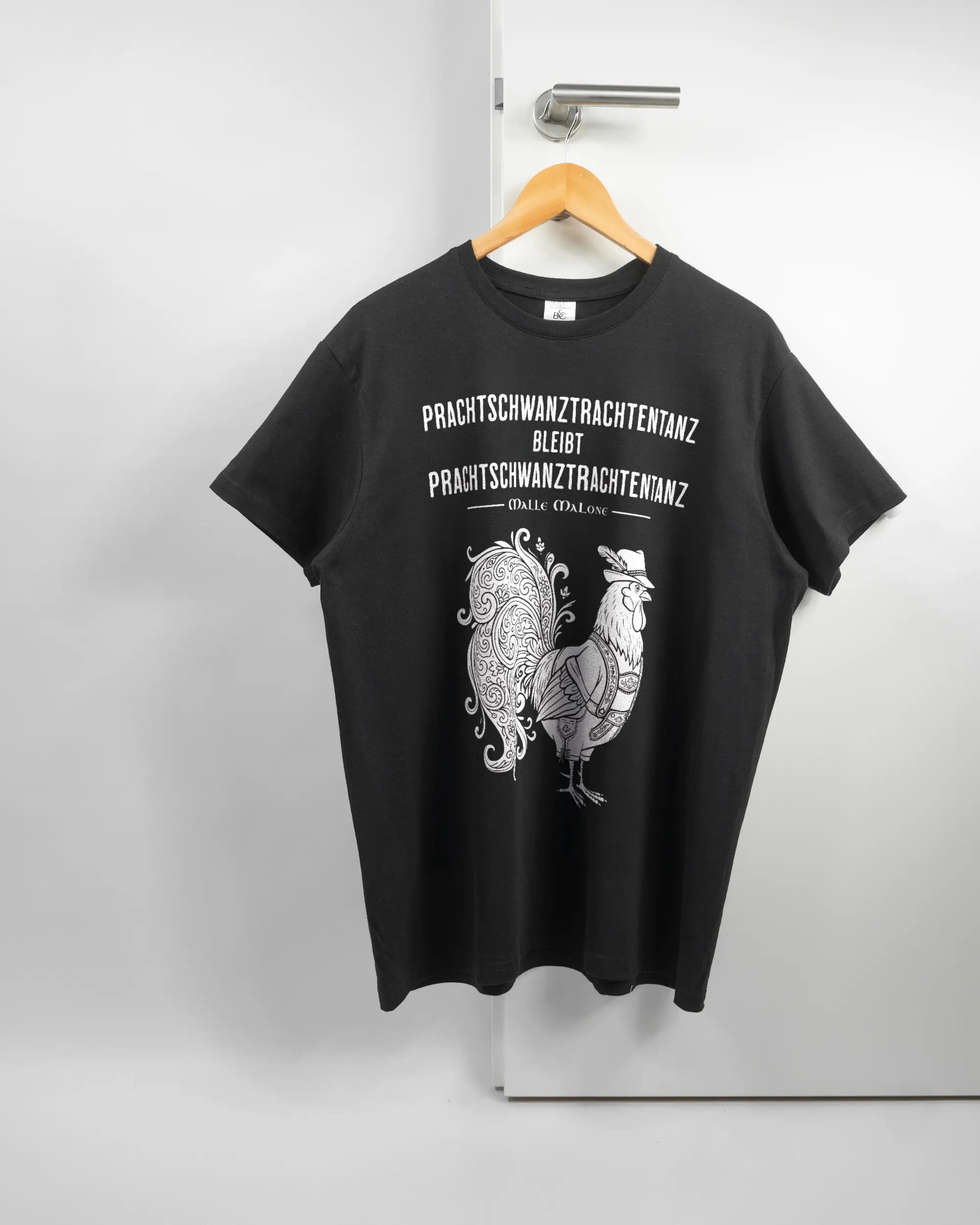 Vorderseite des Basic Unisex T-Shirt Soft von Maondo mit dem Design Trachtentanz in der Farbe Black und in der Größe L auf einem Bügel an der Türklinke aufgehängt