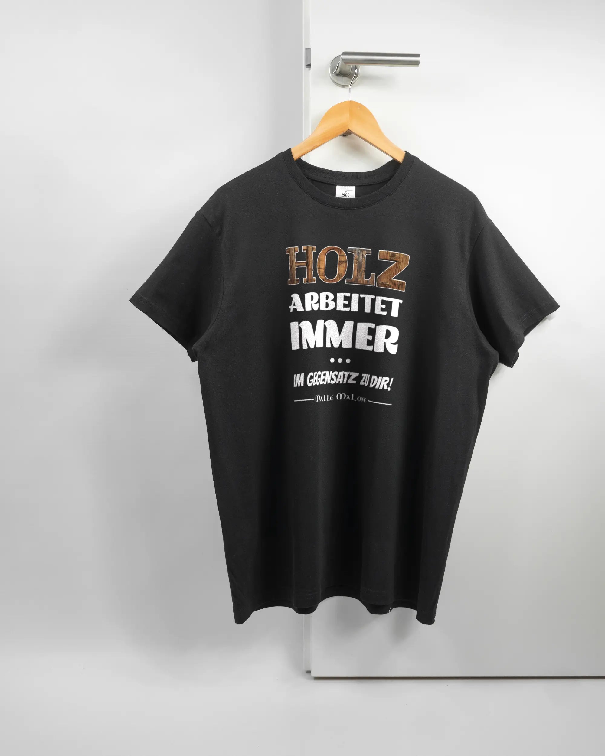 Vorderseite des Basic Unisex T-Shirt Soft von Maondo mit dem Design Holzarbeit in der Farbe Black und in der Größe L auf einem Bügel an der Türklinke aufgehängt