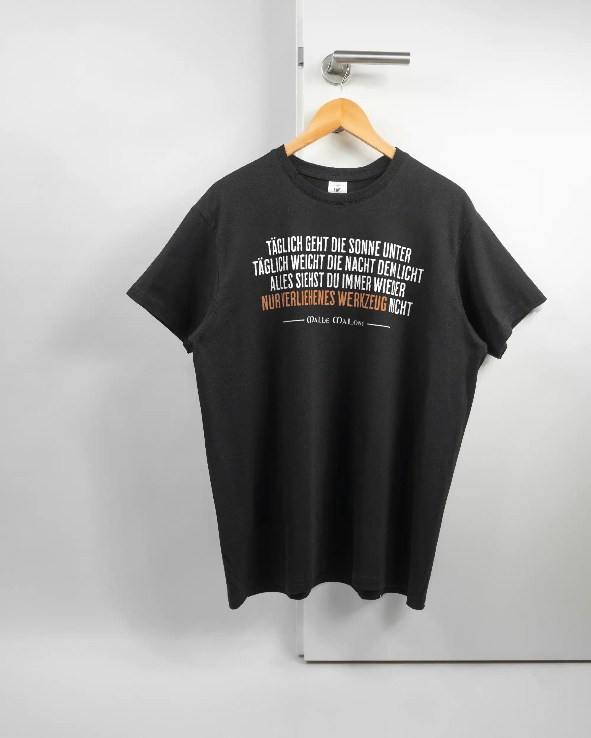Vorderseite des Basic Unisex T-Shirt Soft von Maondo mit dem Design Wegzeug in der Farbe Black und in der Größe L auf einem Bügel an der Türklinke aufgehängt