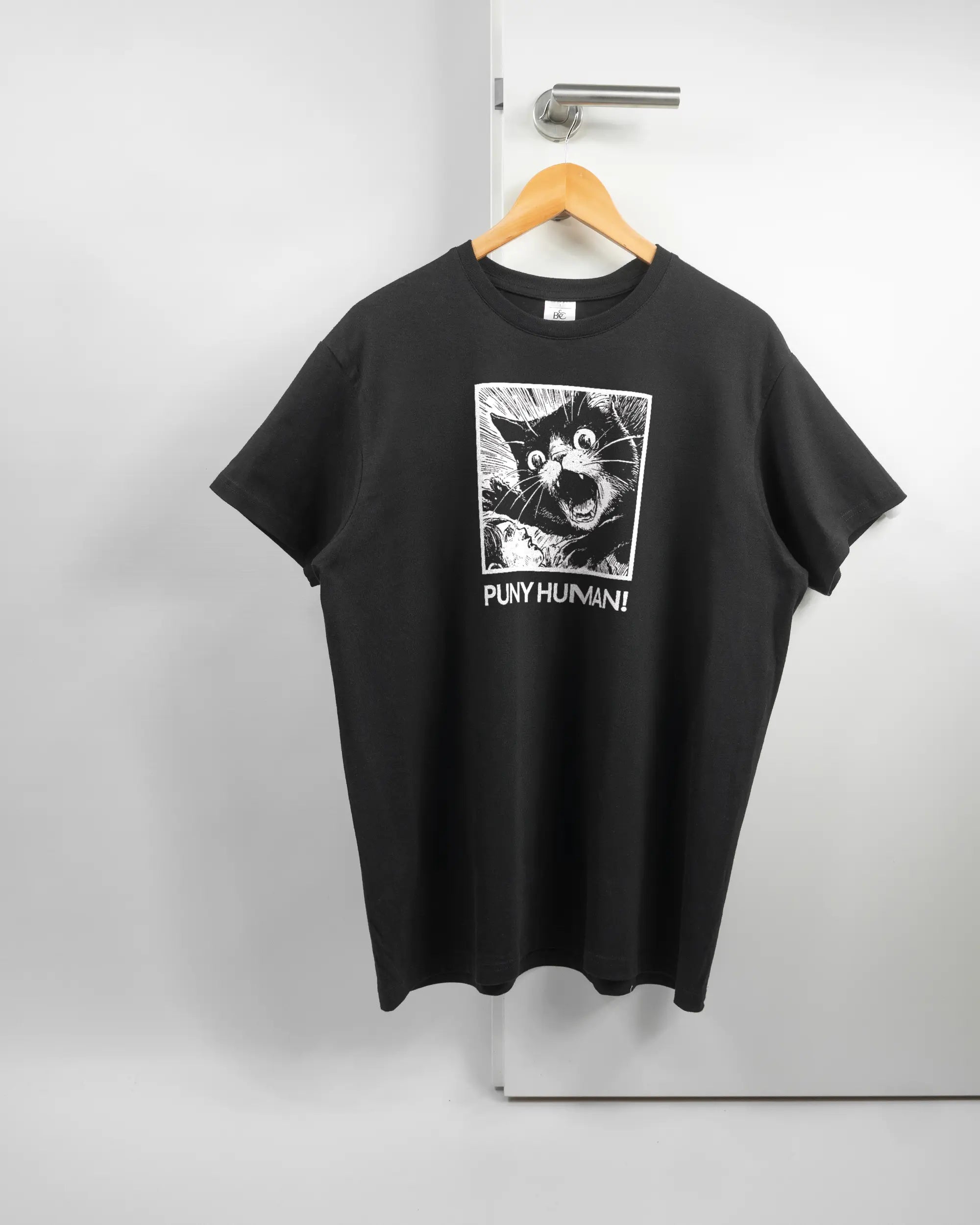 Vorderseite des Basic Unisex T-Shirt Soft von Maondo mit dem Design Puny Human in der Farbe Black und in der Größe L auf einem Bügel an der Türklinke aufgehängt