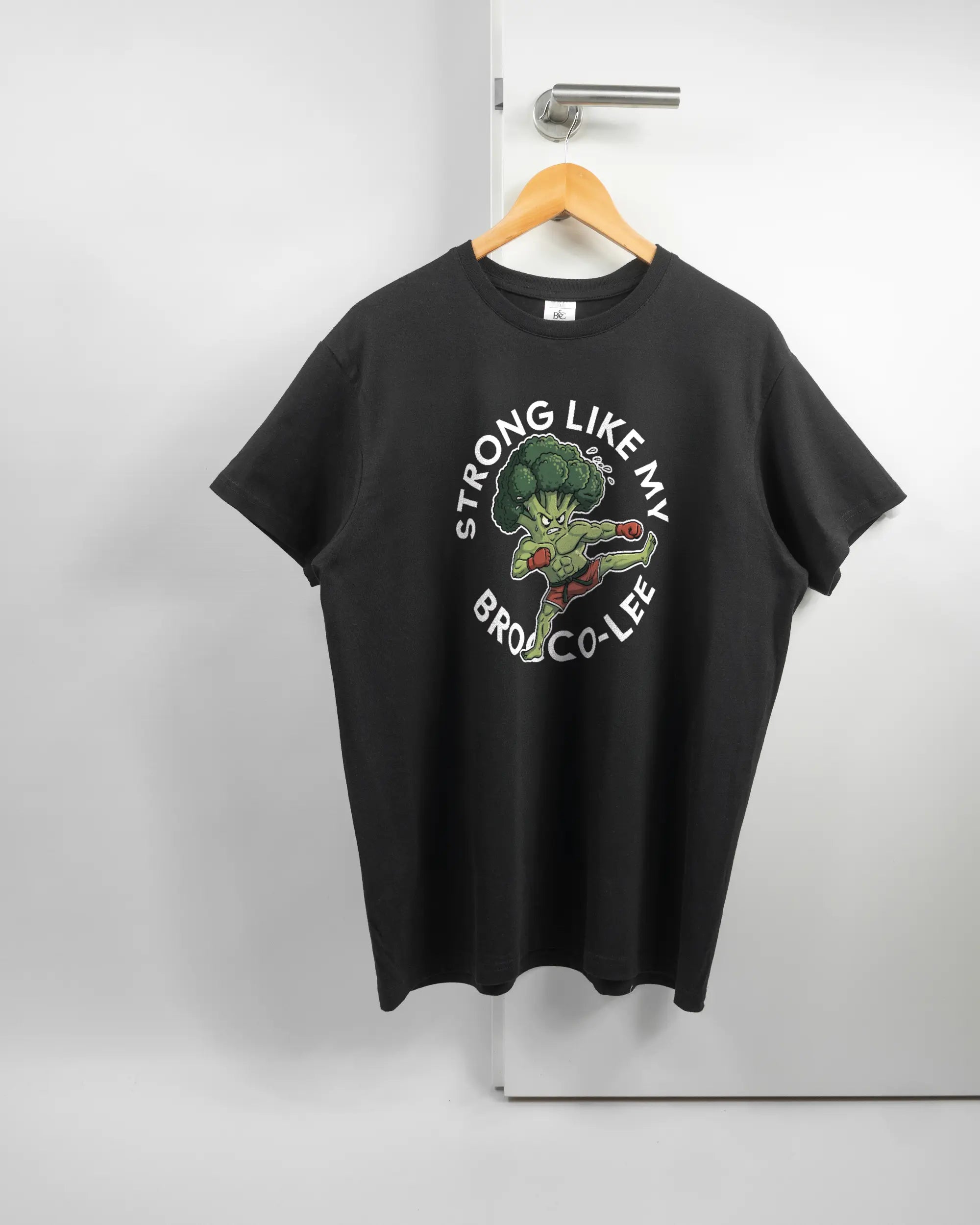 Vorderseite des Basic Unisex T-Shirt Soft von Maondo mit dem Design Brocco-Lee in der Farbe Black und in der Größe L auf einem Bügel an der Türklinke aufgehängt