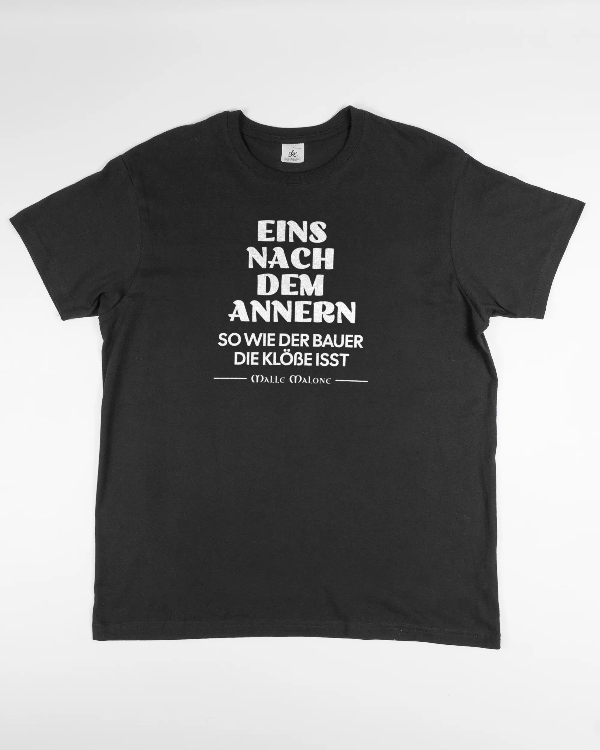 Vorderseite des Basic Unisex T-Shirt Soft von Maondo mit dem Design Eins nach dem Annern in der Farbe Black und in der Größe L flach auf den Boden gelegt