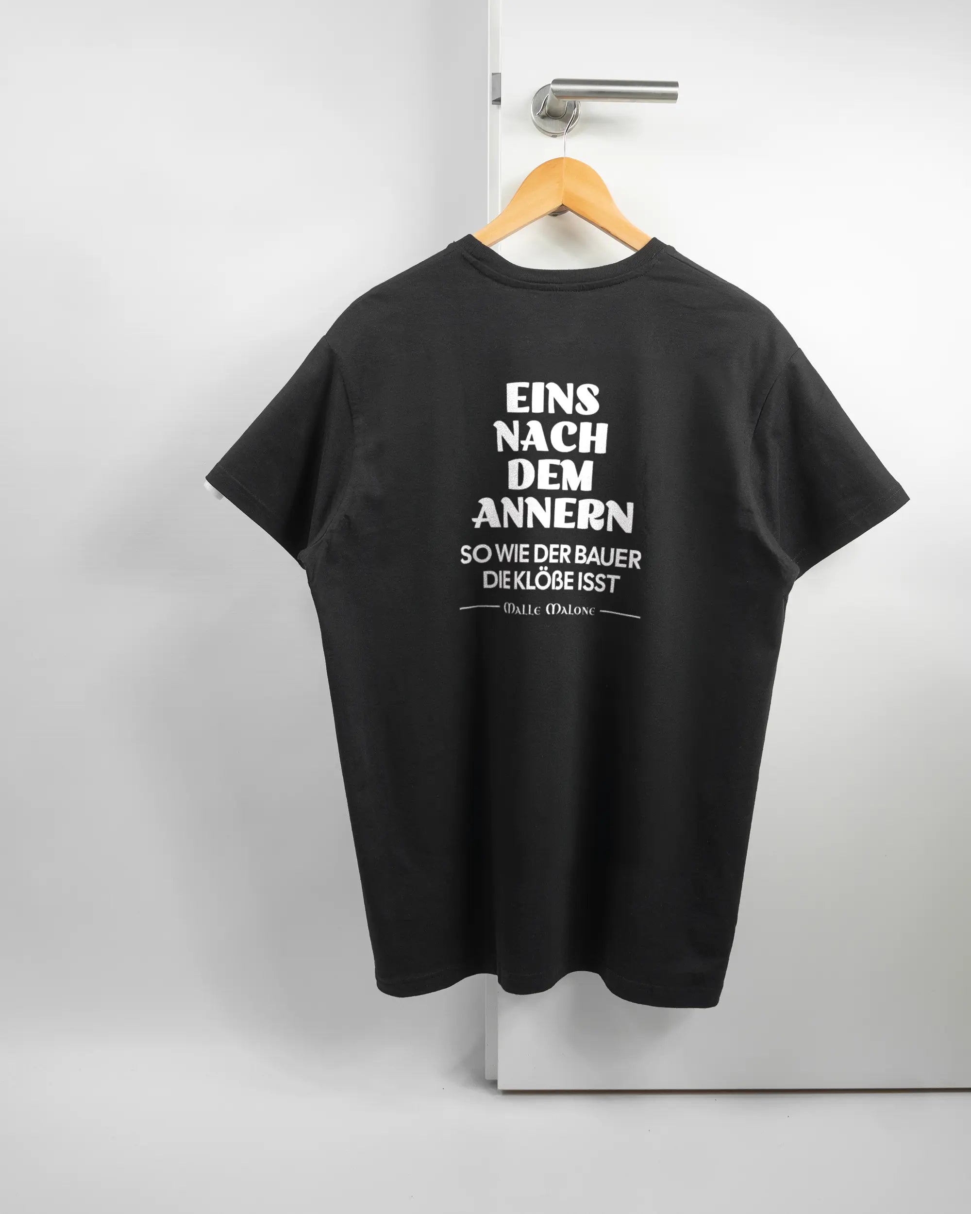 Rückseite des Basic Unisex T-Shirt Soft von Maondo mit dem Design Eins nach dem Annern in der Farbe Black und in der Größe L auf einem Bügel an der Türklinke aufgehängt