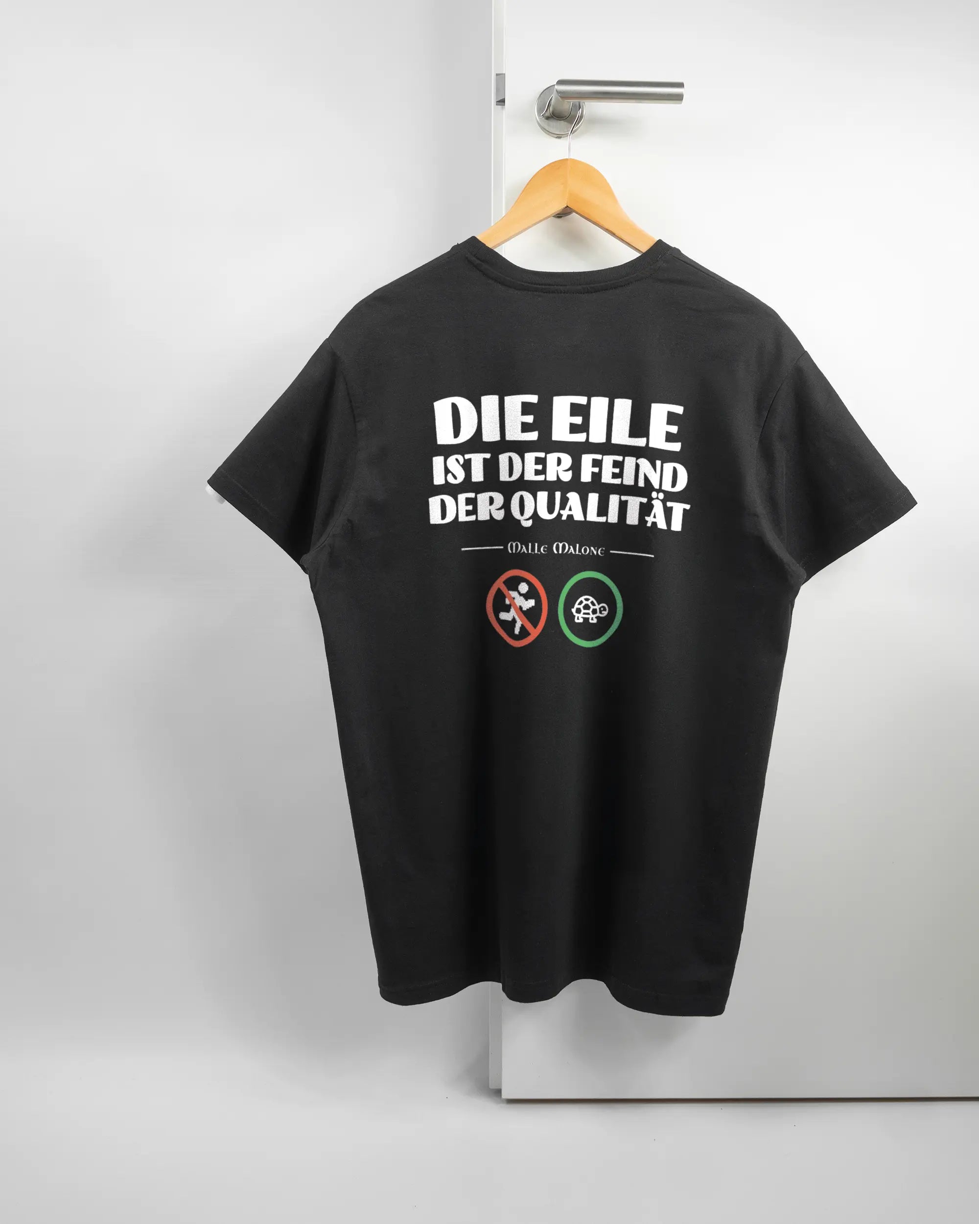 Rückseite des Basic Unisex T-Shirt Soft von Maondo mit dem Design Keine Eile in der Farbe Black und in der Größe L auf einem Bügel an der Türklinke aufgehängt