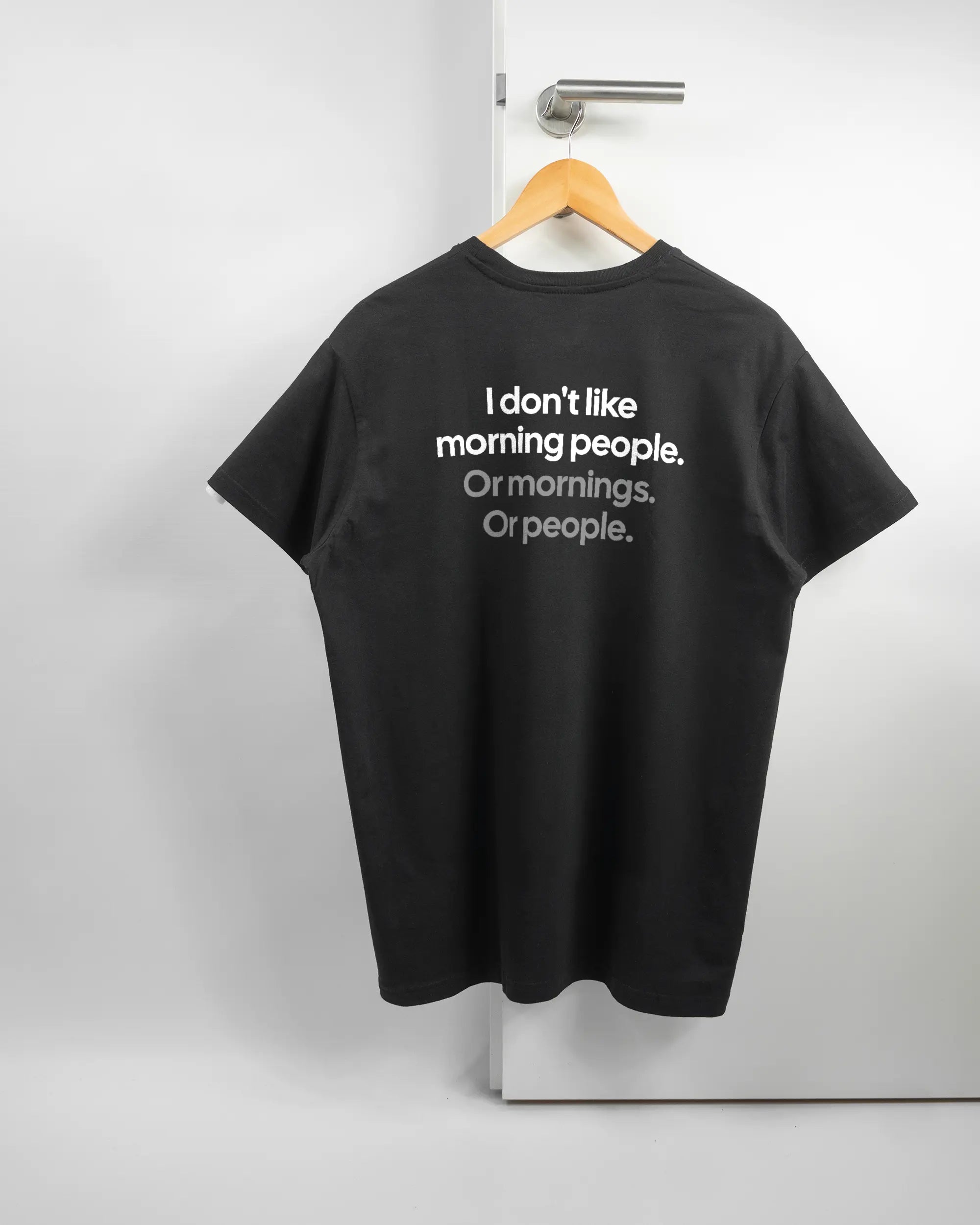 Rückseite des Basic Unisex T-Shirt Soft von Maondo mit dem Design Morning Person in der Farbe Black und in der Größe L auf einem Bügel an der Türklinke aufgehängt