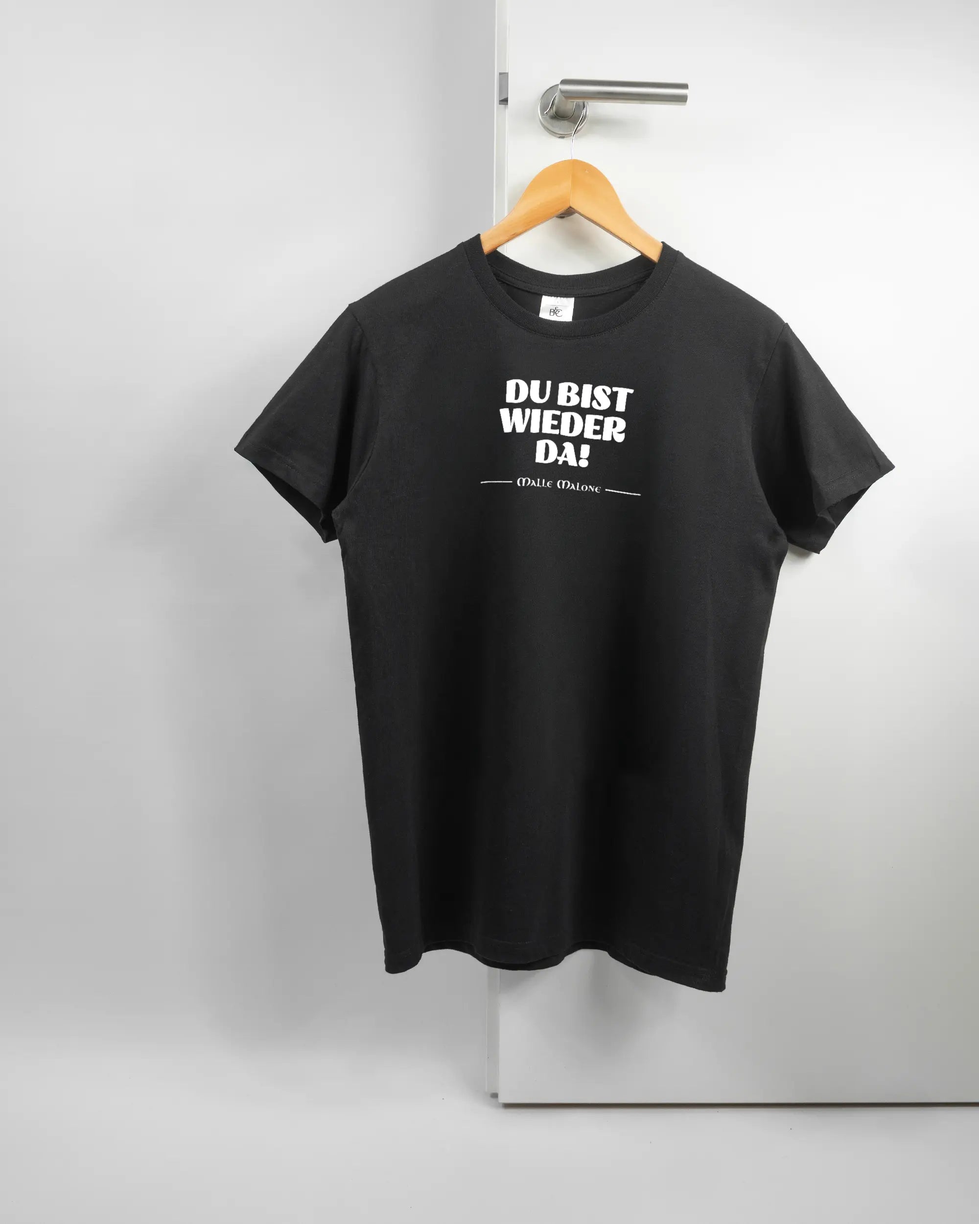 Vorderseite des Basic Unisex T-Shirt Soft von Maondo mit dem Design Wieder da in der Farbe Black und in der Größe S auf einem Bügel an der Türklinke aufgehängt