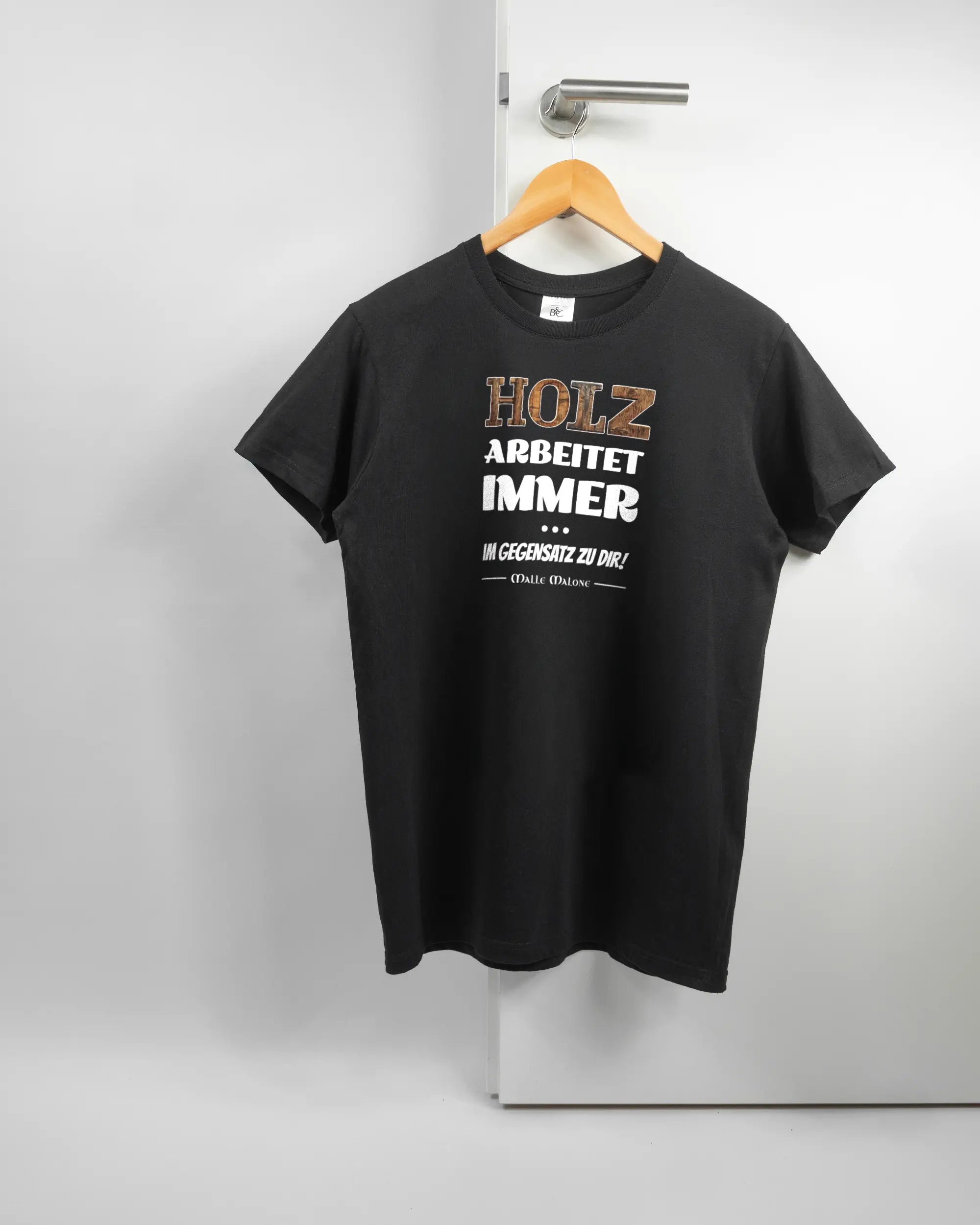 Vorderseite des Basic Unisex T-Shirt Soft von Maondo mit dem Design Holzarbeit in der Farbe Black und in der Größe S auf einem Bügel an der Türklinke aufgehängt
