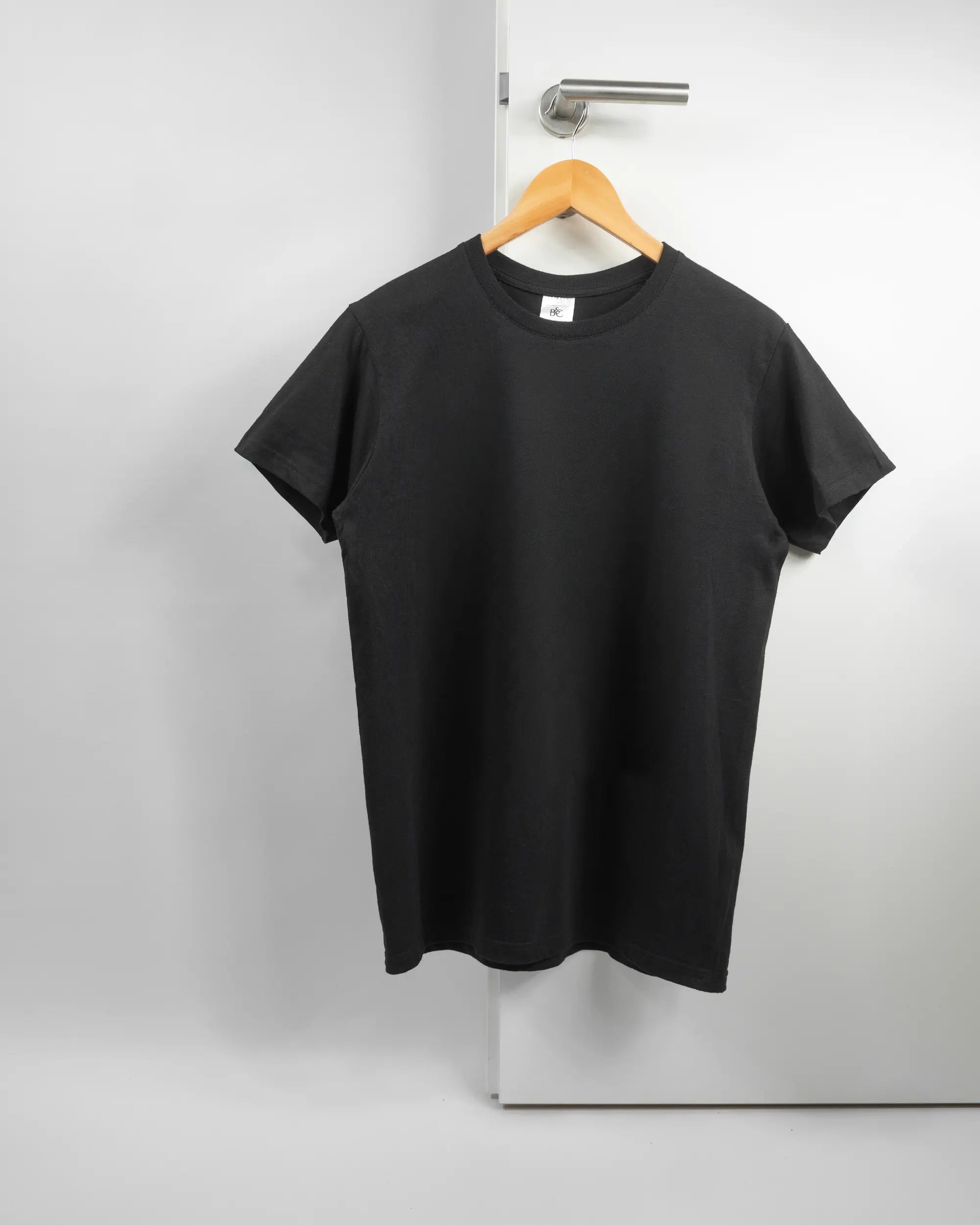 Vorderseite des Basic Unisex T-Shirt Soft von Maondo ohne Motiv in der Farbe Black und in der Größe S auf einem Bügel an der Türklinke aufgehängt