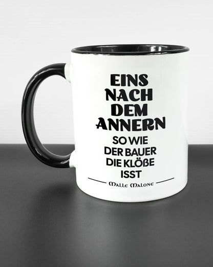 Titelbild, das die linke Seite der beidseitig bedruckten Keramiktasse von Maondo mit dem Design Eins nach dem Annern in der Farbe Duotone auf einem Holztisch zeigt