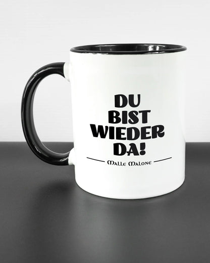 Titelbild, das die linke Seite der beidseitig bedruckten Keramiktasse von Maondo mit dem Design Wieder da in der Farbe Duotone auf einem Holztisch zeigt