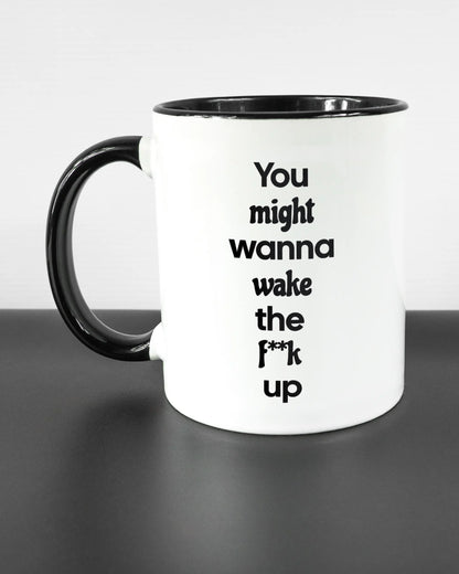 Titelbild, das die linke Seite der beidseitig bedruckten Keramiktasse von Maondo mit dem Design Wanna Wake in der Farbe Duotone auf einem Holztisch zeigt