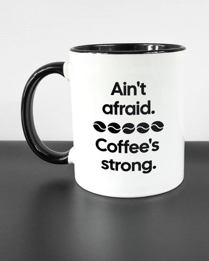 Titelbild, das die linke Seite der beidseitig bedruckten Keramiktasse von Maondo mit dem Design Coffee is strong in der Farbe Duotone auf einem Holztisch zeigt