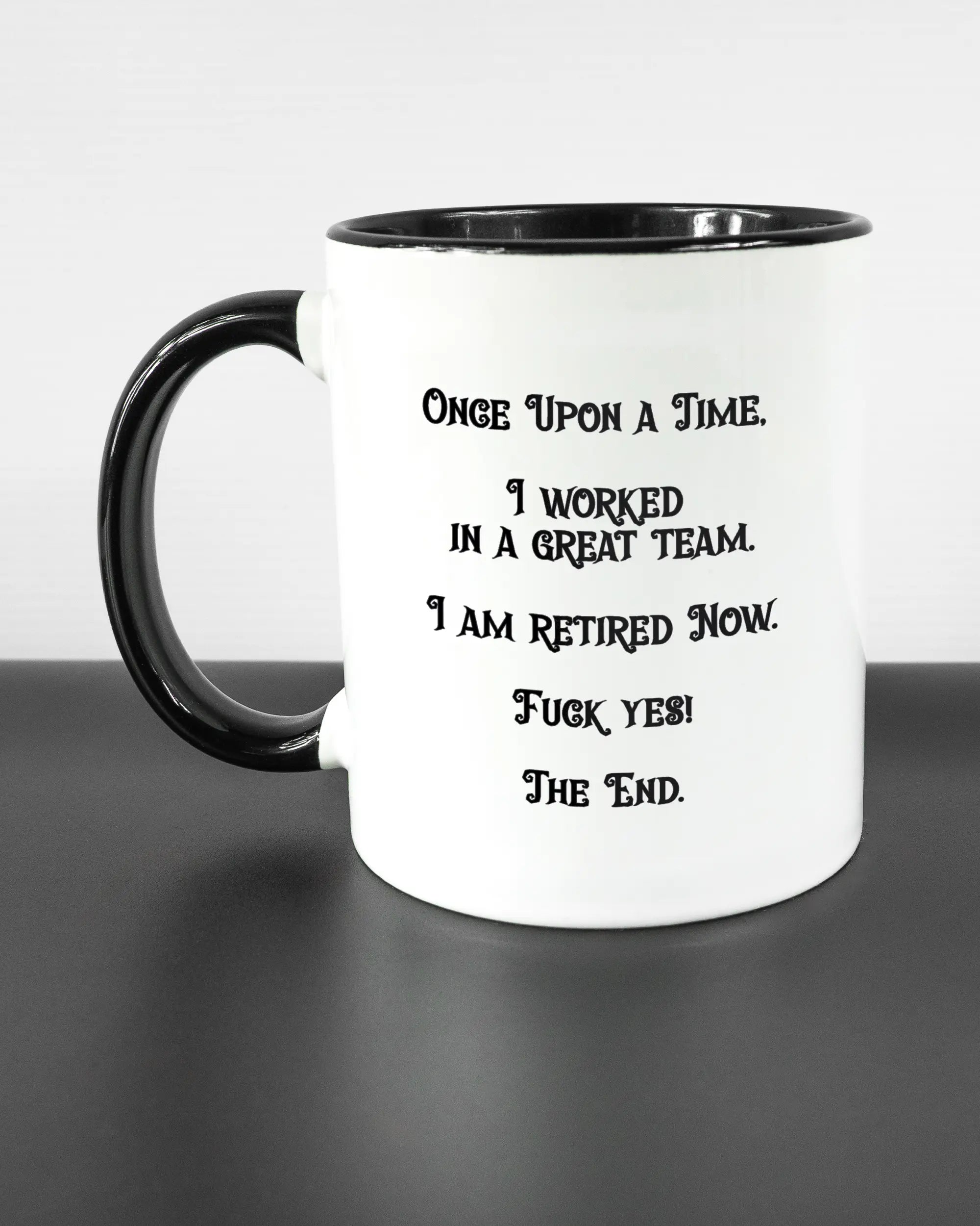 Titelbild, das die linke Seite der beidseitig bedruckten Keramiktasse von Maondo mit dem Design Finally Retired in der Farbe Duotone auf einem Holztisch zeigt