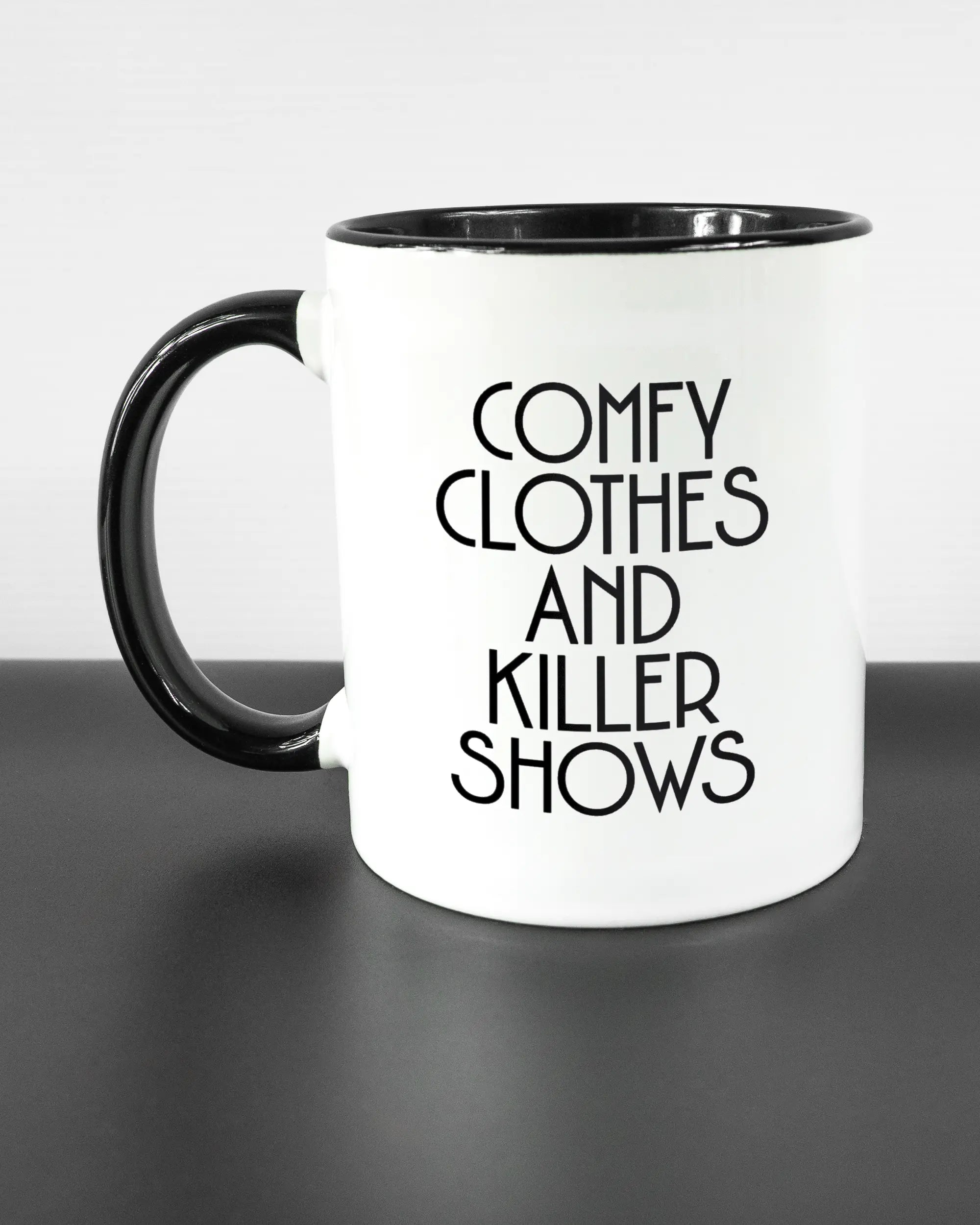 Titelbild, das die linke Seite der beidseitig bedruckten Keramiktasse von Maondo mit dem Design Killer Shows in der Farbe Duotone auf einem Holztisch zeigt