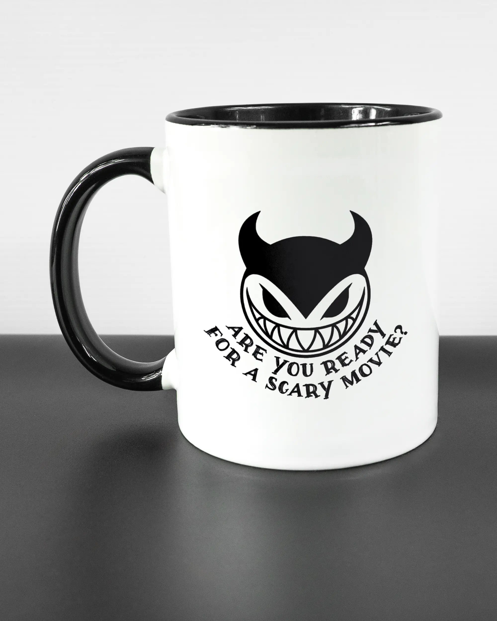 Titelbild, das die linke Seite der beidseitig bedruckten Keramiktasse von Maondo mit dem Design Scary Movie in der Farbe Duotone auf einem Holztisch zeigt
