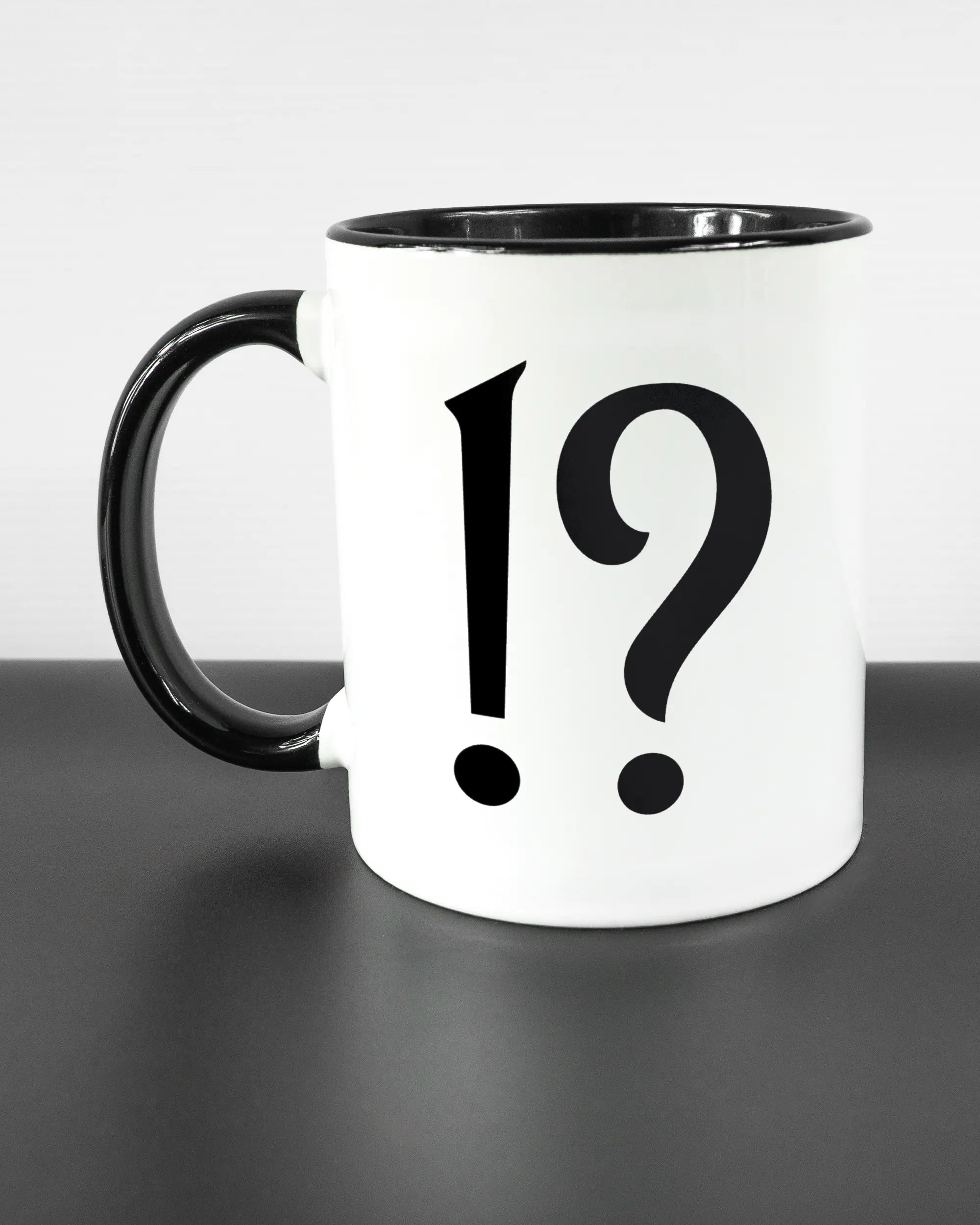 Titelbild, das die linke Seite der beidseitig bedruckten Keramiktasse von Maondo mit dem Design WHAT in der Farbe Duotone auf einem Holztisch zeigt