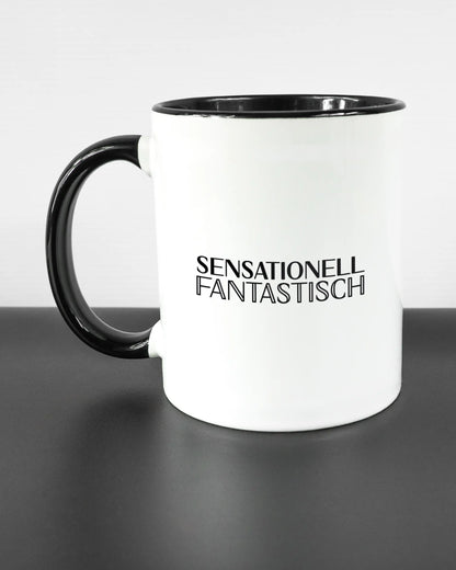 Titelbild, das die linke Seite der beidseitig bedruckten Keramiktasse von Maondo mit dem Design Sensationell in der Farbe Duotone auf einem Holztisch zeigt