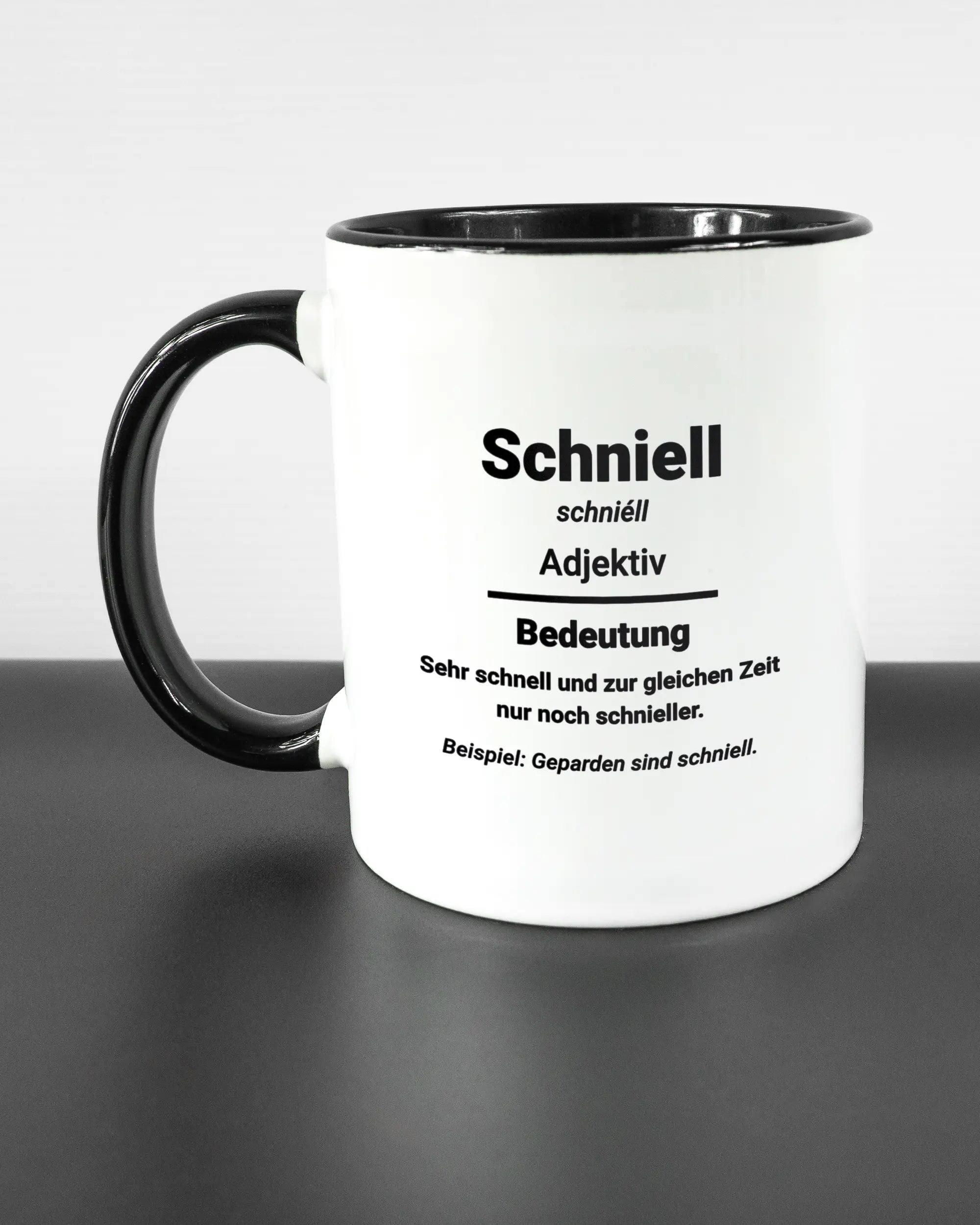 Titelbild, das die linke Seite der beidseitig bedruckten Keramiktasse von Maondo mit dem Design Schniell in der Farbe Duotone auf einem Holztisch zeigt