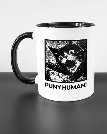 Titelbild, das die linke Seite der beidseitig bedruckten Keramiktasse von Maondo mit dem Design Puny Human in der Farbe Duotone auf einem Holztisch zeigt