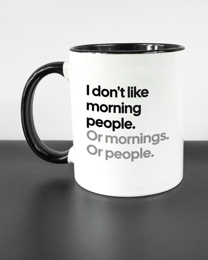 Titelbild, das die linke Seite der beidseitig bedruckten Keramiktasse von Maondo mit dem Design Morning Person in der Farbe Duotone auf einem Holztisch zeigt