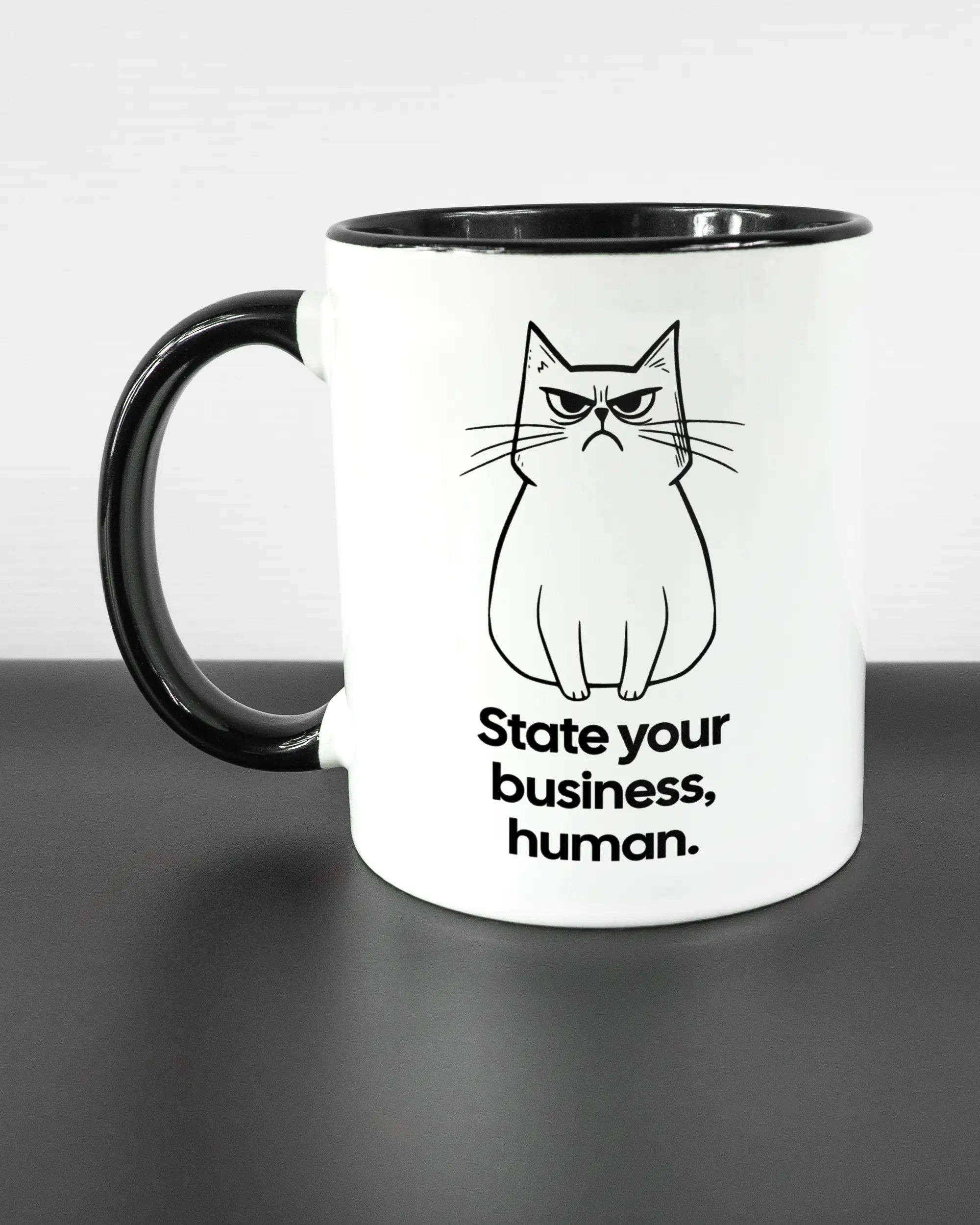 Titelbild, das die linke Seite der beidseitig bedruckten Keramiktasse von Maondo mit dem Design Grumpy Purr in der Farbe Duotone auf einem Holztisch zeigt
