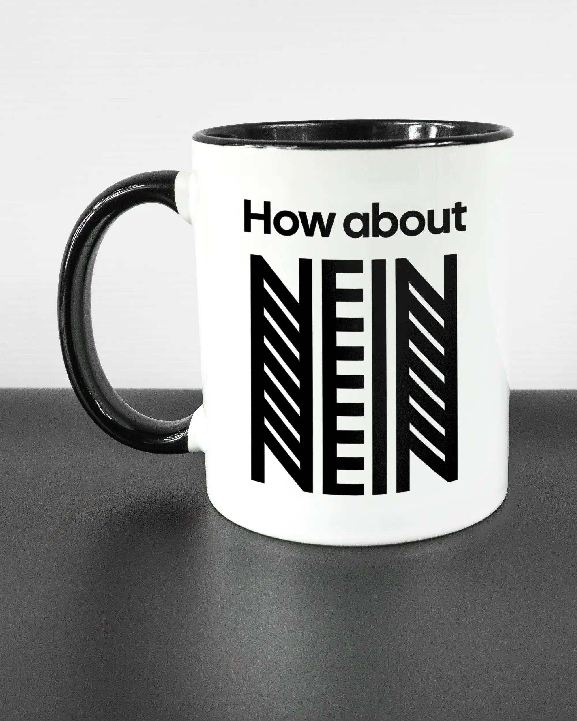 Titelbild, das die linke Seite der beidseitig bedruckten Keramiktasse von Maondo mit dem Design How about nein in der Farbe Duotone auf einem Holztisch zeigt