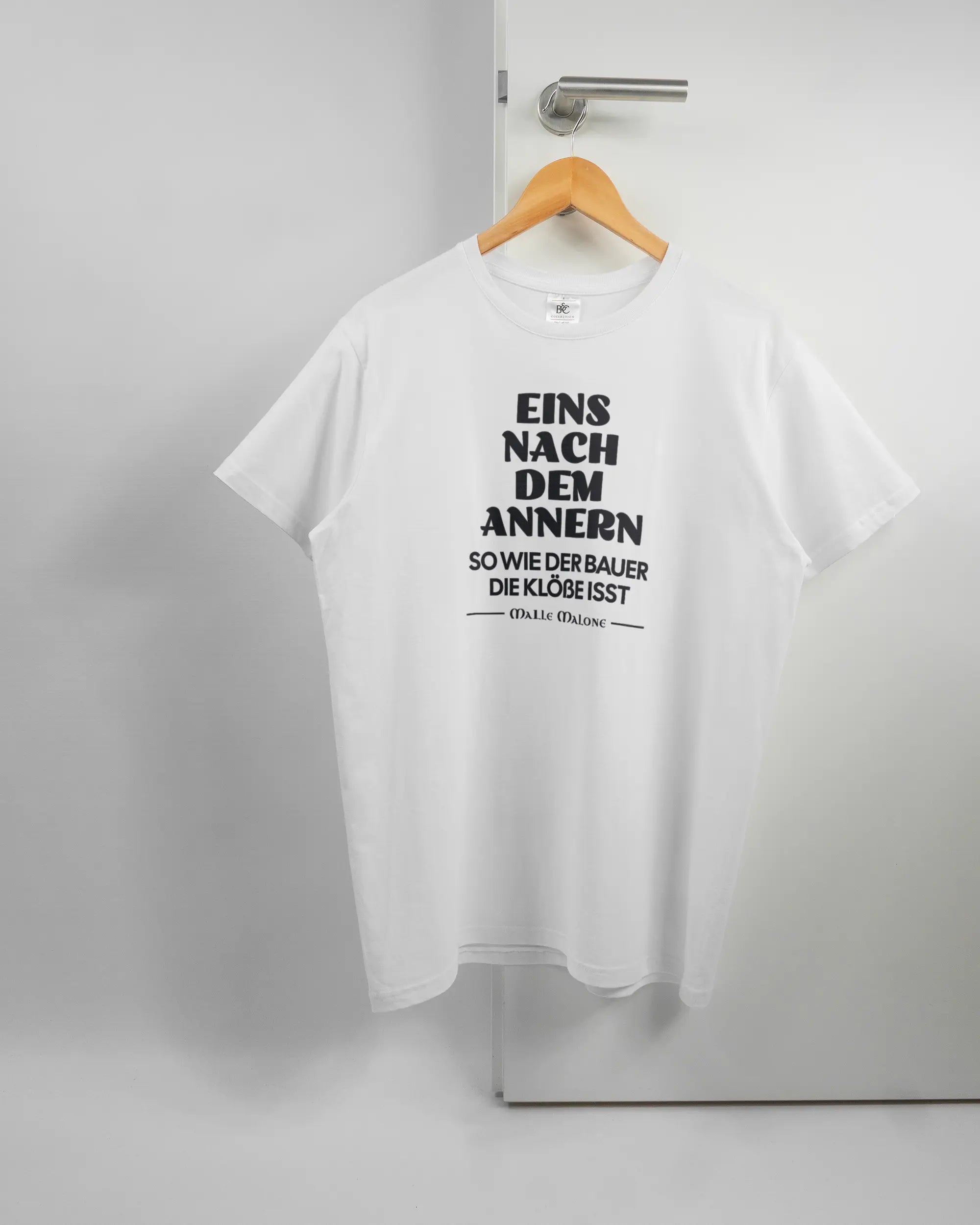 Vorderseite des Basic Unisex T-Shirt Soft von Maondo mit dem Design Eins nach dem Annern in der Farbe White und in der Größe L auf einem Bügel an der Türklinke aufgehängt