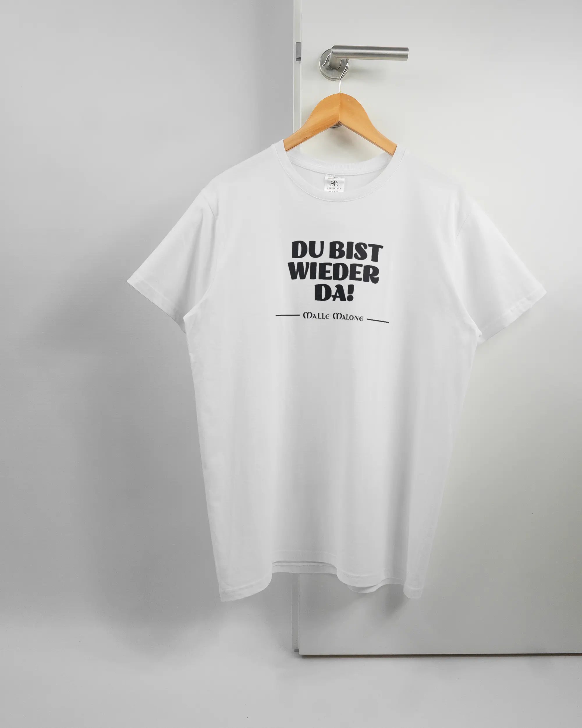 Vorderseite des Basic Unisex T-Shirt Soft von Maondo mit dem Design Wieder da in der Farbe White und in der Größe L auf einem Bügel an der Türklinke aufgehängt