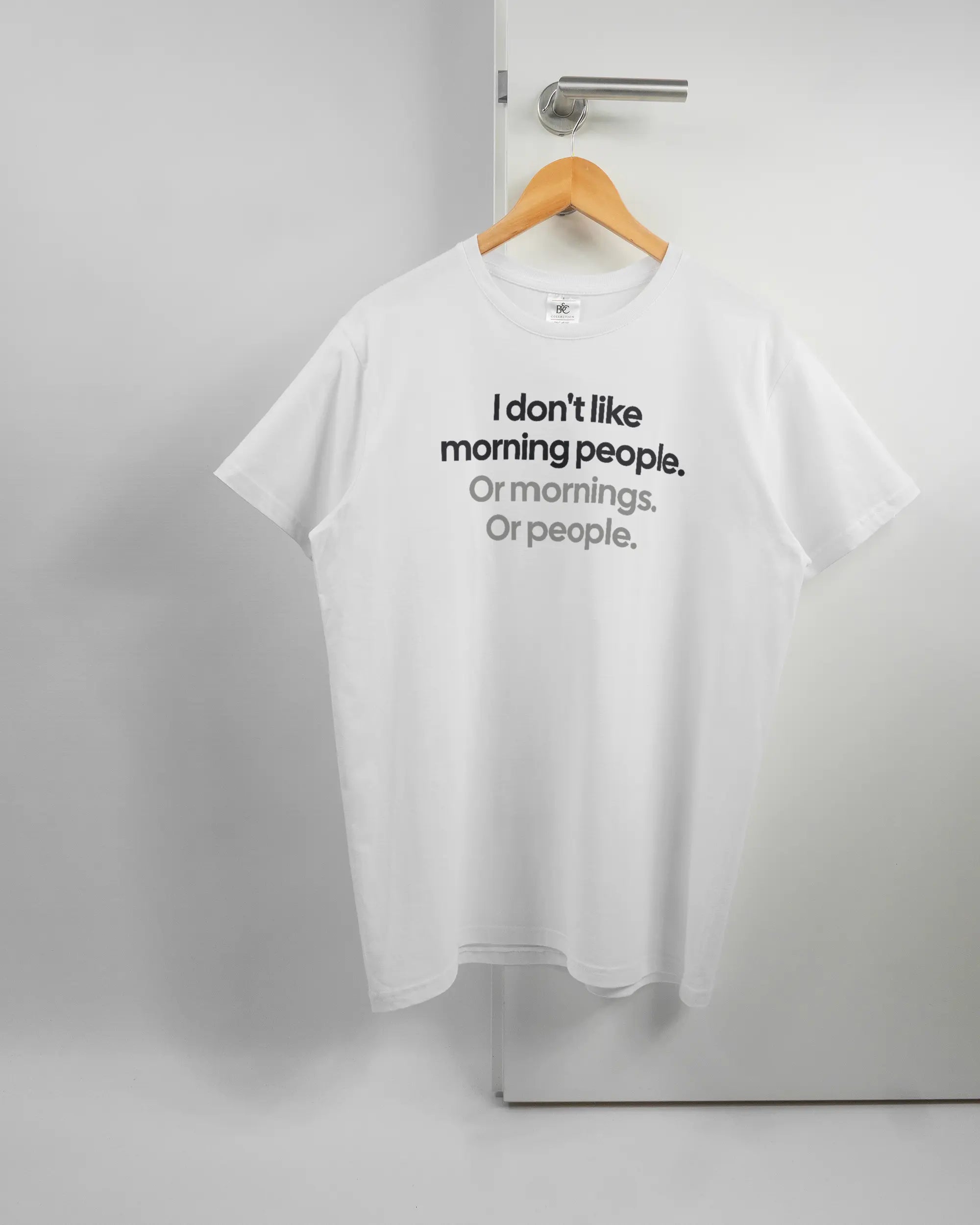 Vorderseite des Basic Unisex T-Shirt Soft von Maondo mit dem Design Morning Person in der Farbe White und in der Größe L auf einem Bügel an der Türklinke aufgehängt