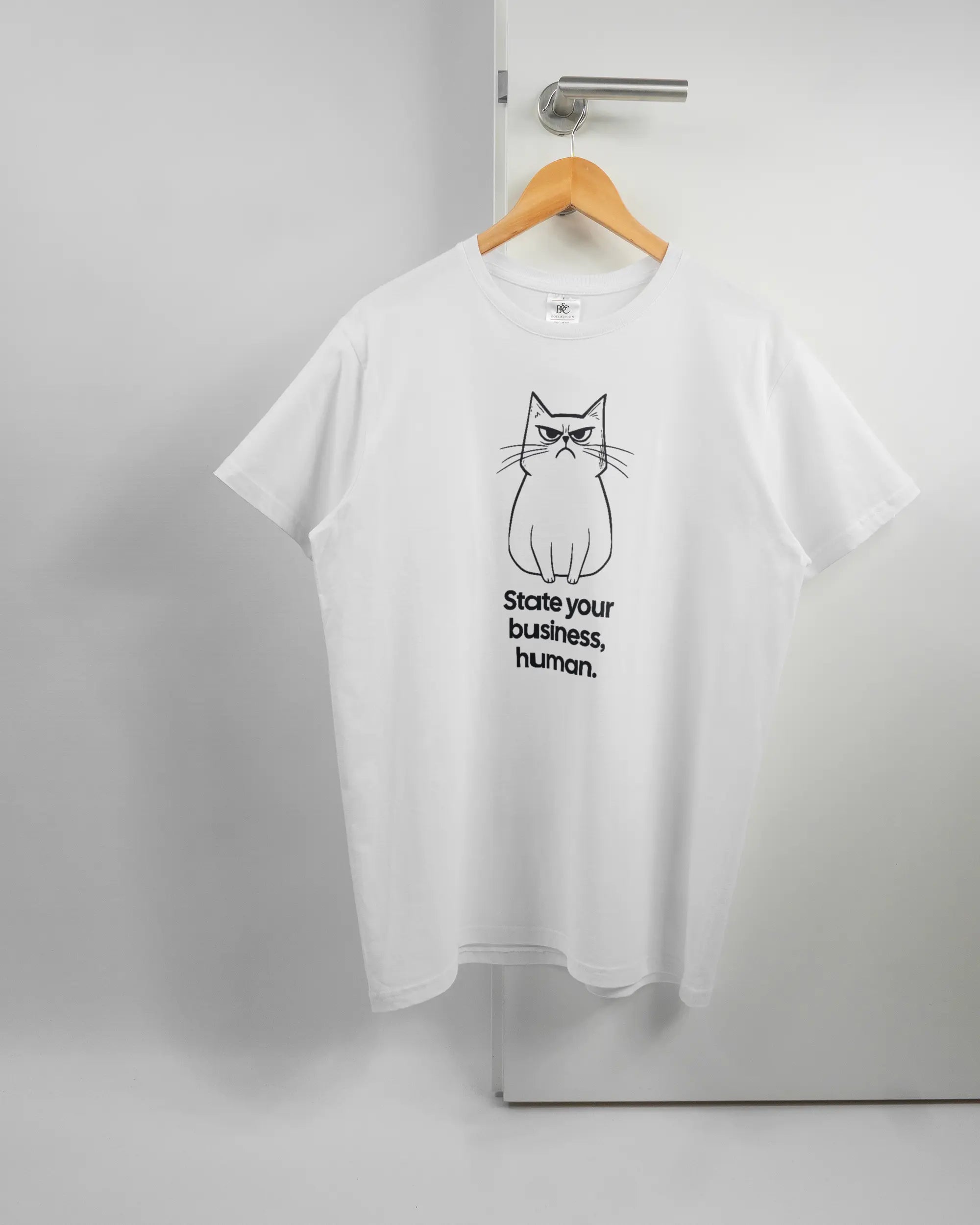Vorderseite des Basic Unisex T-Shirt Soft von Maondo mit dem Design Grumpy Purr in der Farbe White und in der Größe L auf einem Bügel an der Türklinke aufgehängt