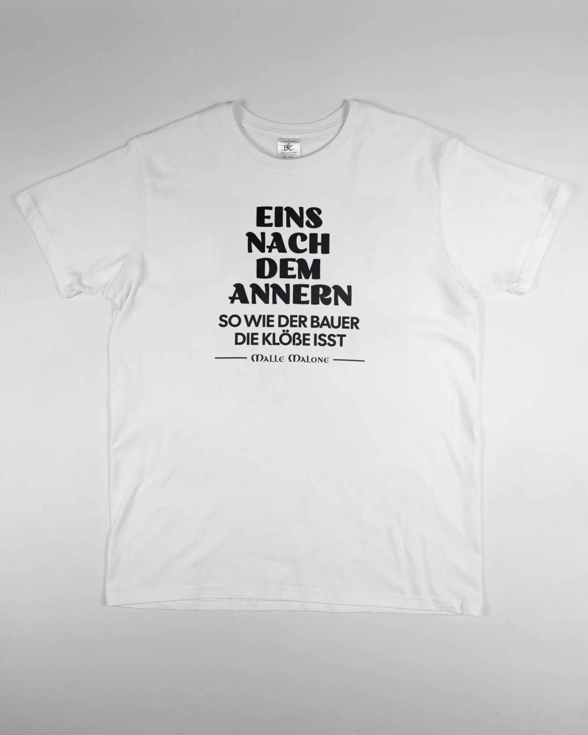 Vorderseite des Basic Unisex T-Shirt Soft von Maondo mit dem Design Eins nach dem Annern in der Farbe White und in der Größe L flach auf den Boden gelegt