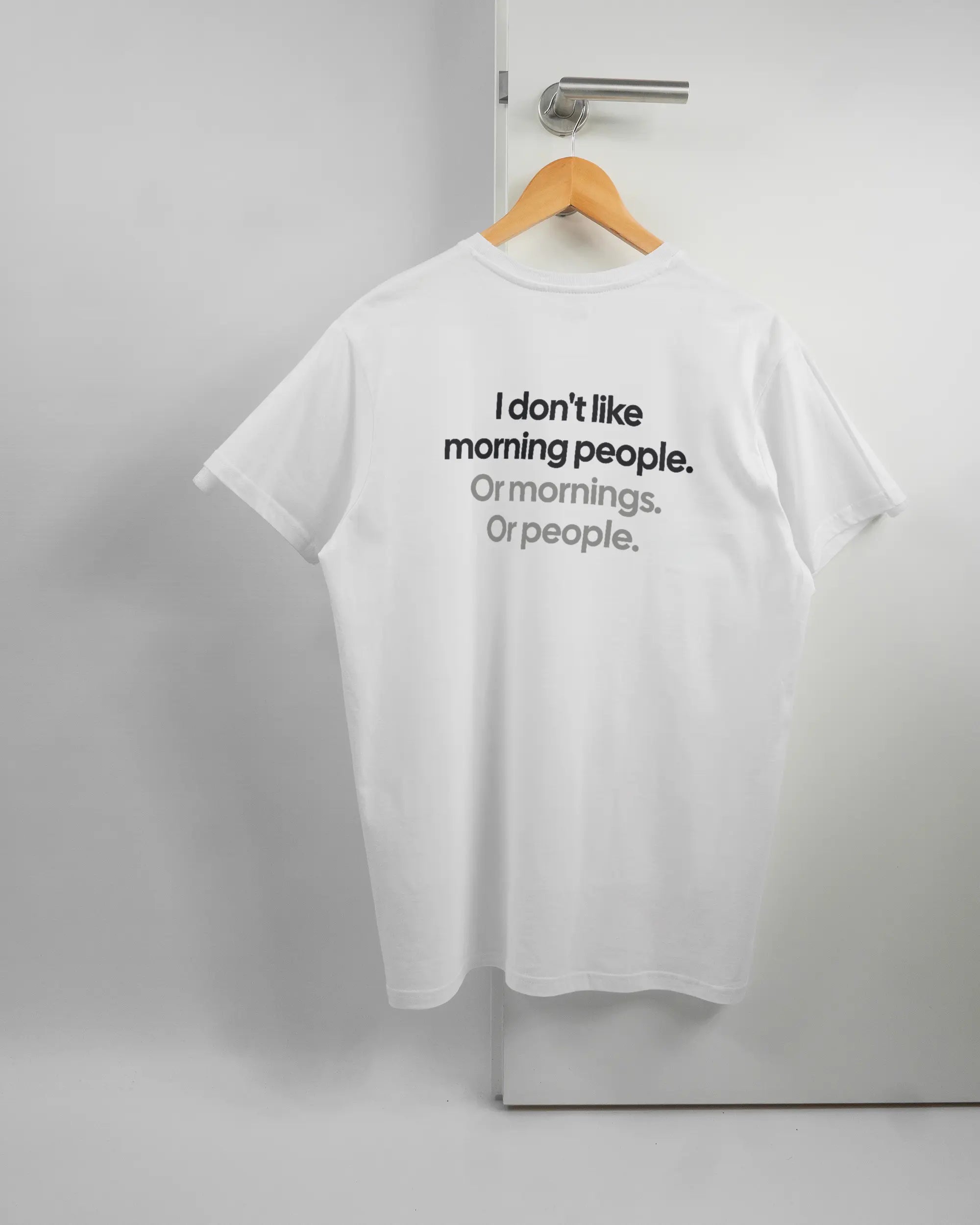 Rückseite des Basic Unisex T-Shirt Soft von Maondo mit dem Design Morning Person in der Farbe White und in der Größe L auf einem Bügel an der Türklinke aufgehängt