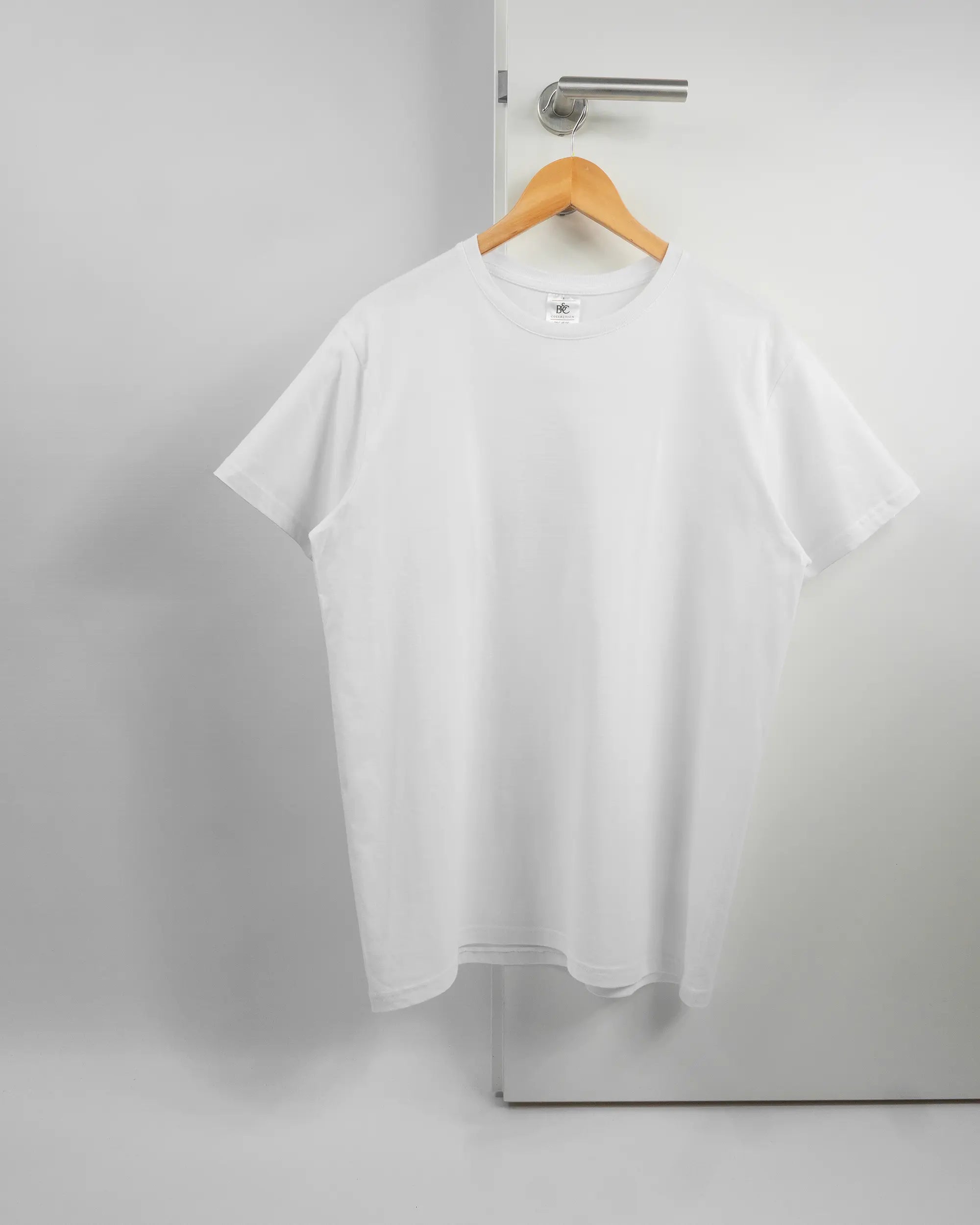 Vorderseite des Basic Unisex T-Shirt Soft von Maondo ohne Motiv in der Farbe White und in der Größe L auf einem Bügel an der Türklinke aufgehängt