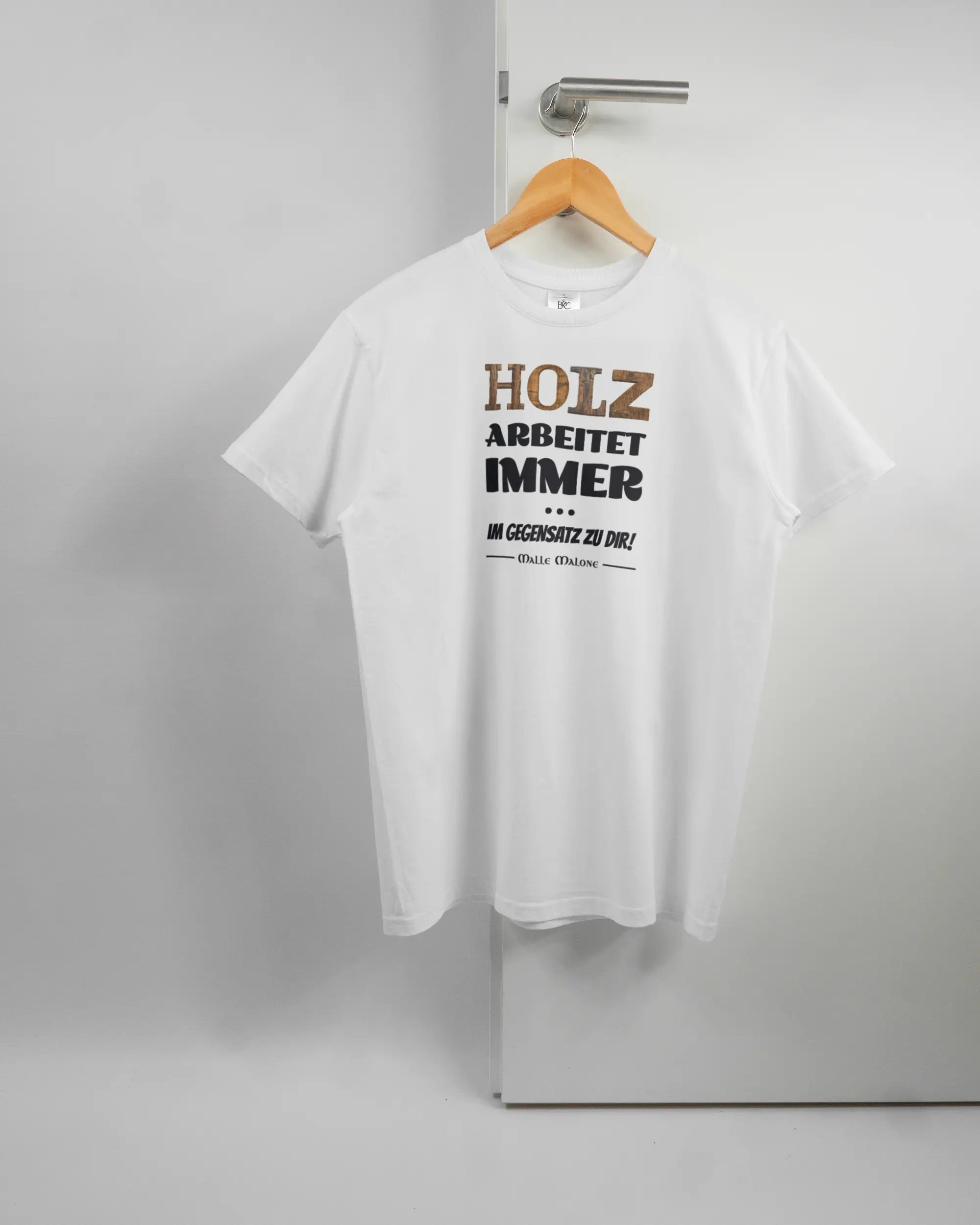 Vorderseite des Basic Unisex T-Shirt Soft von Maondo mit dem Design Holzarbeit in der Farbe White und in der Größe S auf einem Bügel an der Türklinke aufgehängt
