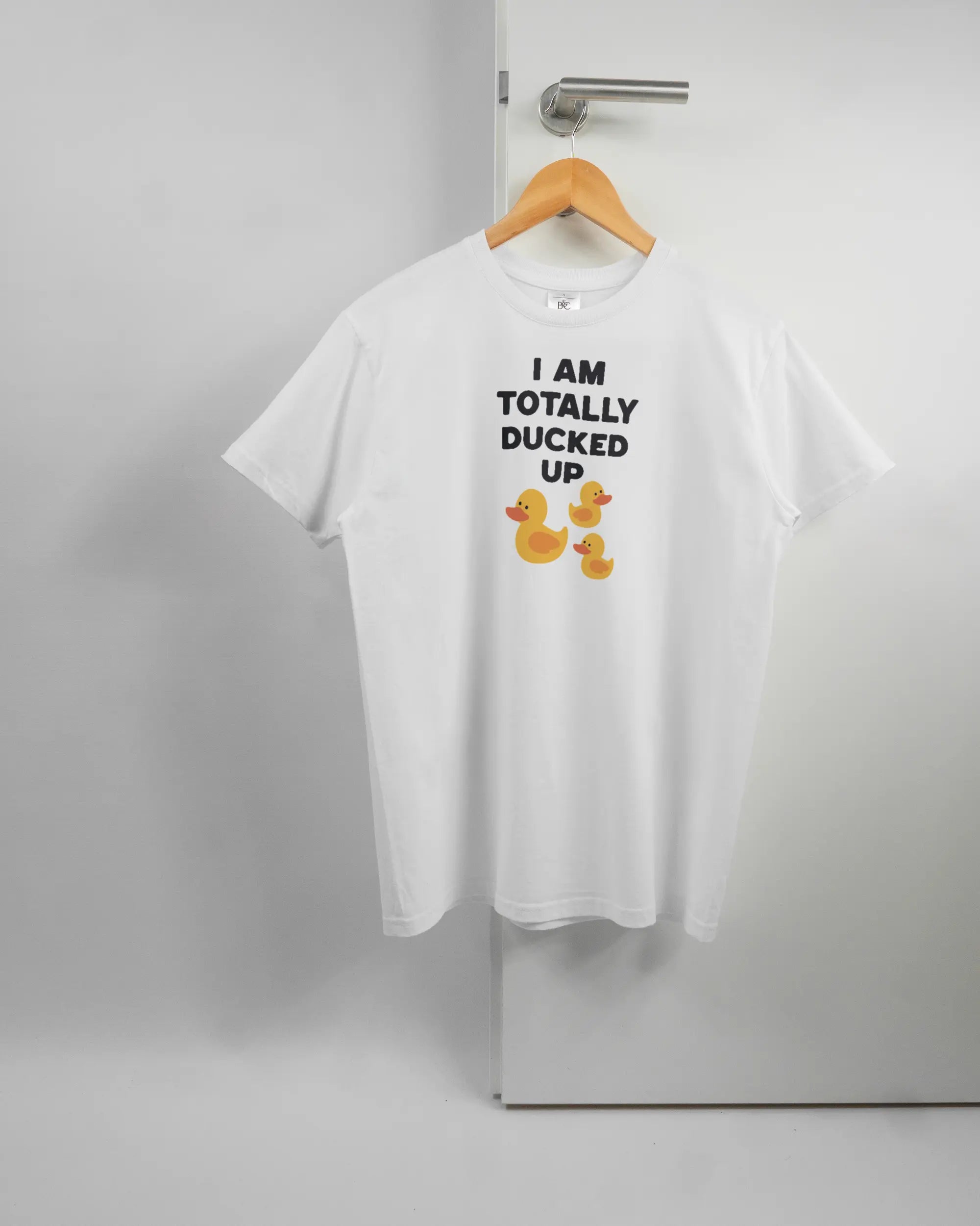 Vorderseite des Basic Unisex T-Shirt Soft von Maondo mit dem Design Ducked Up in der Farbe White und in der Größe S auf einem Bügel an der Türklinke aufgehängt