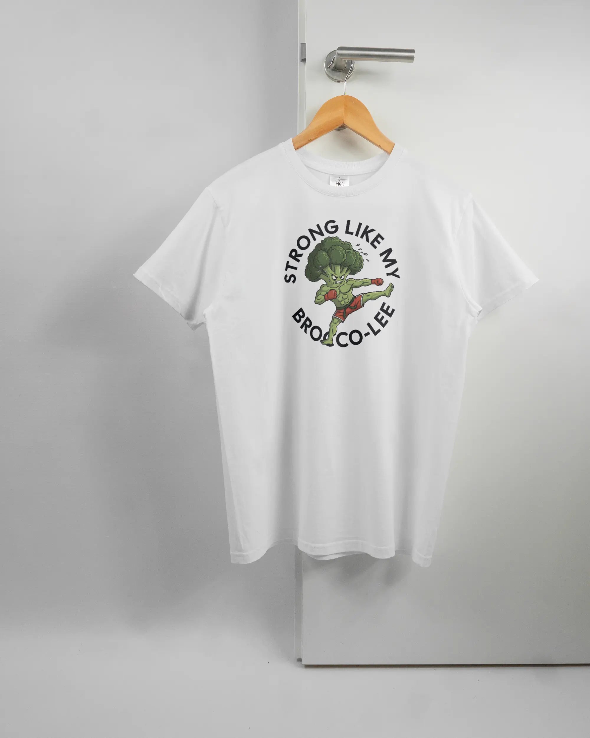 Vorderseite des Basic Unisex T-Shirt Soft von Maondo mit dem Design Brocco-Lee in der Farbe White und in der Größe S auf einem Bügel an der Türklinke aufgehängt