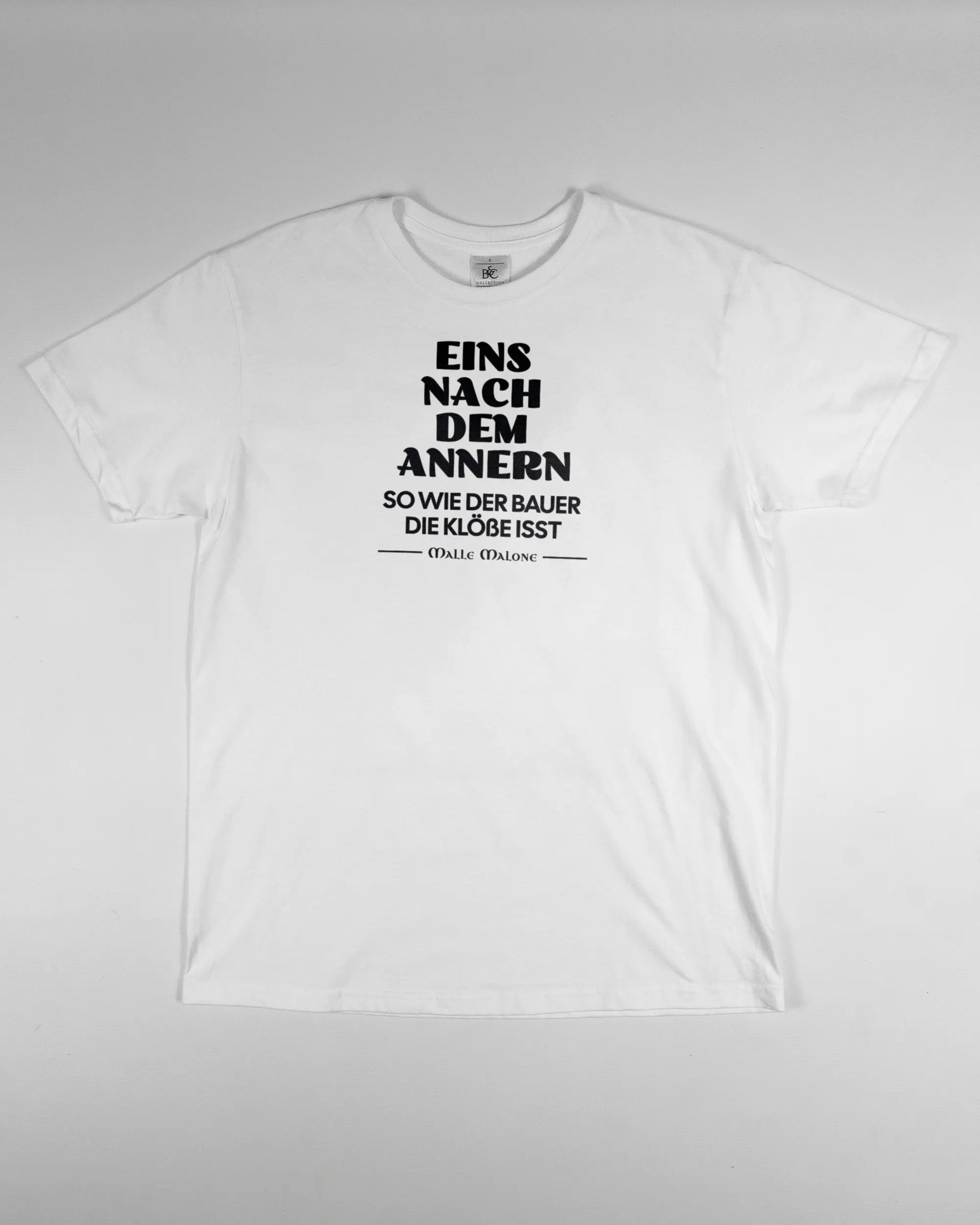 Vorderseite des Basic Unisex T-Shirt Soft von Maondo mit dem Design Eins nach dem Annern in der Farbe White und in der Größe S flach auf den Boden gelegt