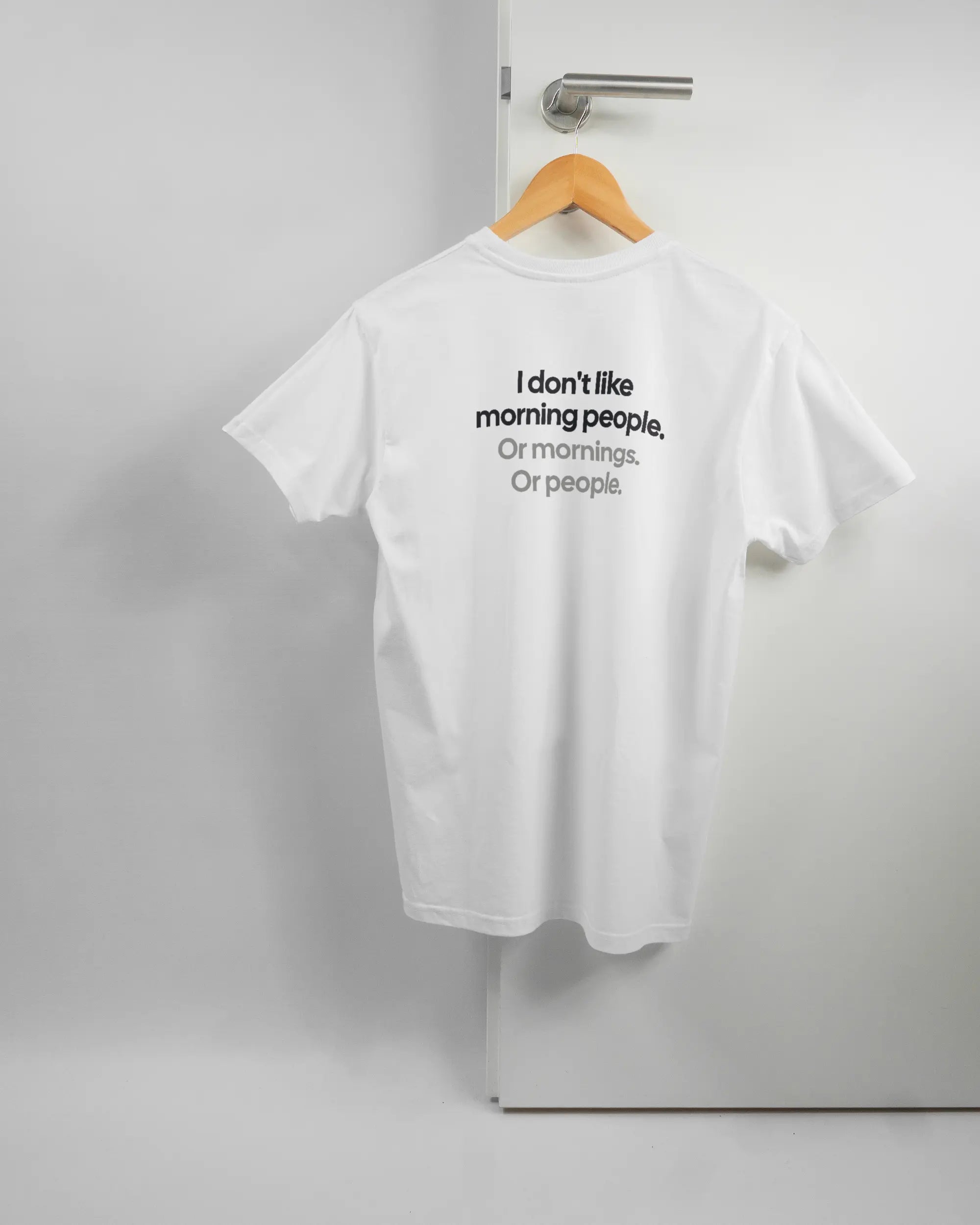Rückseite des Basic Unisex T-Shirt Soft von Maondo mit dem Design Morning Person in der Farbe White und in der Größe S auf einem Bügel an der Türklinke aufgehängt