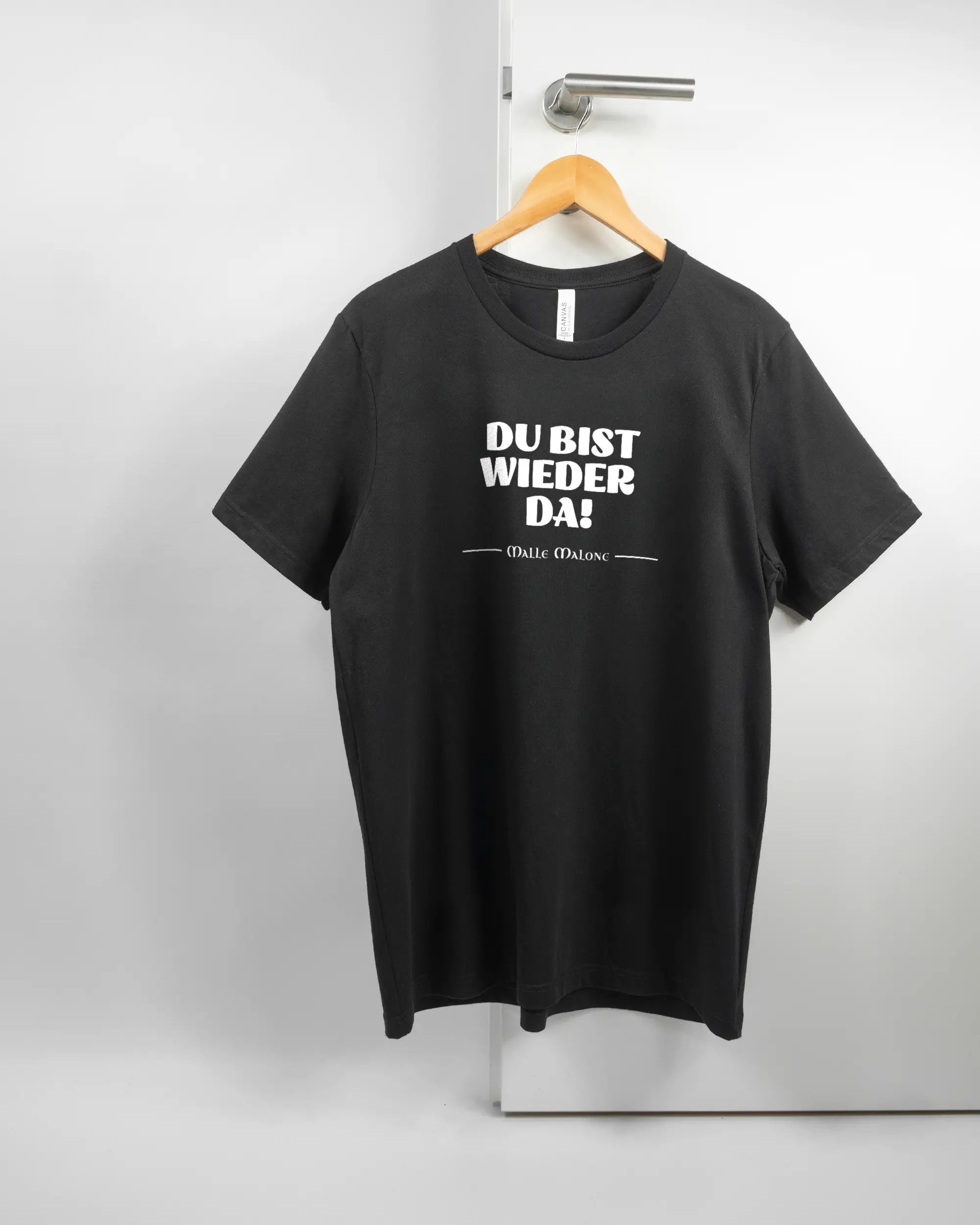 Vorderseite des Basic Unisex T-Shirt Light von Maondo mit dem Design Wieder da in der Farbe Black und in der Größe L auf einem Bügel an der Türklinke aufgehängt